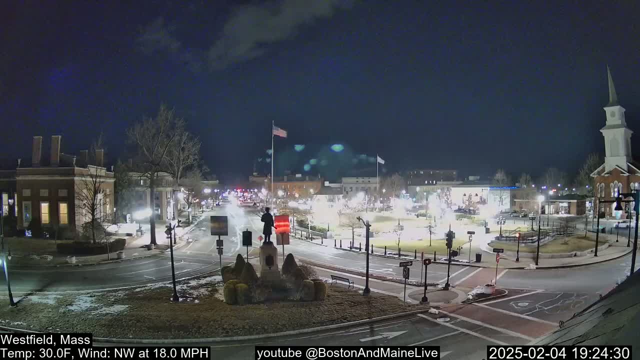 A nighttime view of a town square with a statue at its center, under a clear sky with a 30°F temperature and a northwest wind of 18 mph.