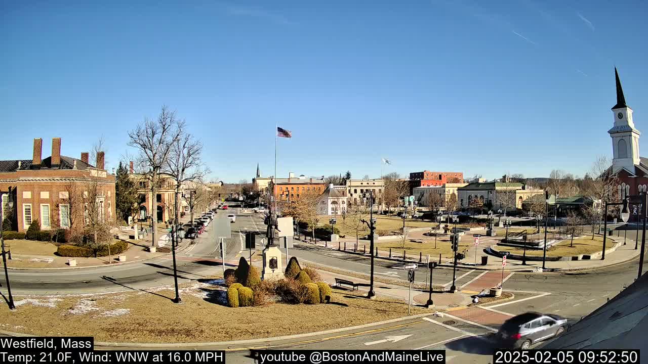 A town square with brick buildings, a monument, and a church steeple is visible on a sunny day with a wind of 16 mph.