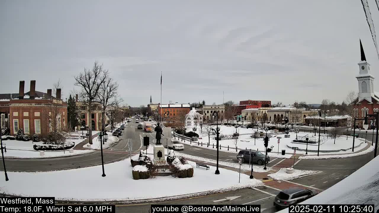 A snow-covered town square with cars and buildings, under an overcast sky.