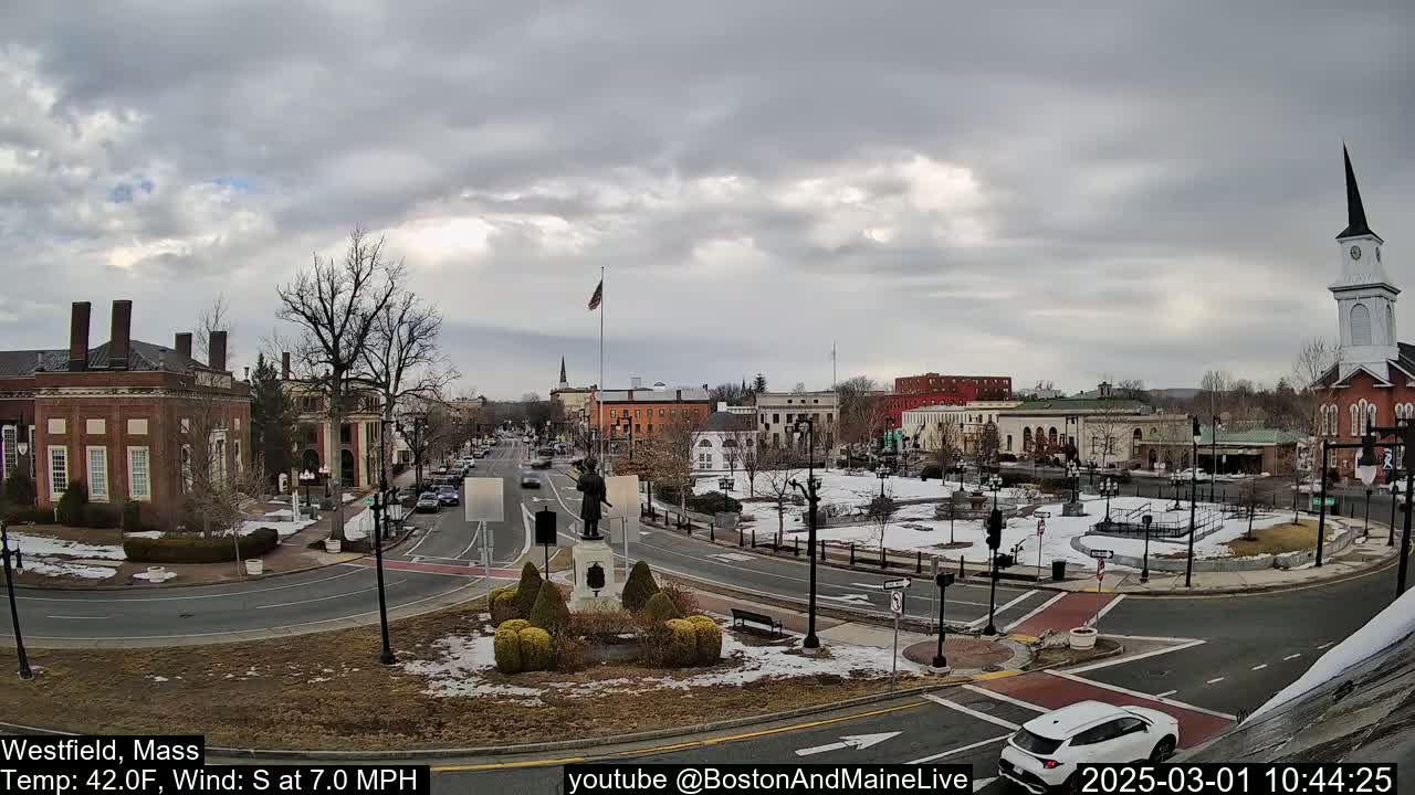 A town square with brick buildings, a statue, and a church under a cloudy sky.