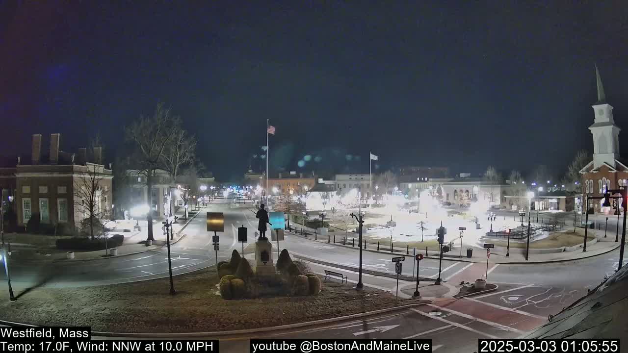 A nighttime view of a town square with a statue in the center, under a clear, dark sky with a 17°F temperature and a 10 mph northwest wind.