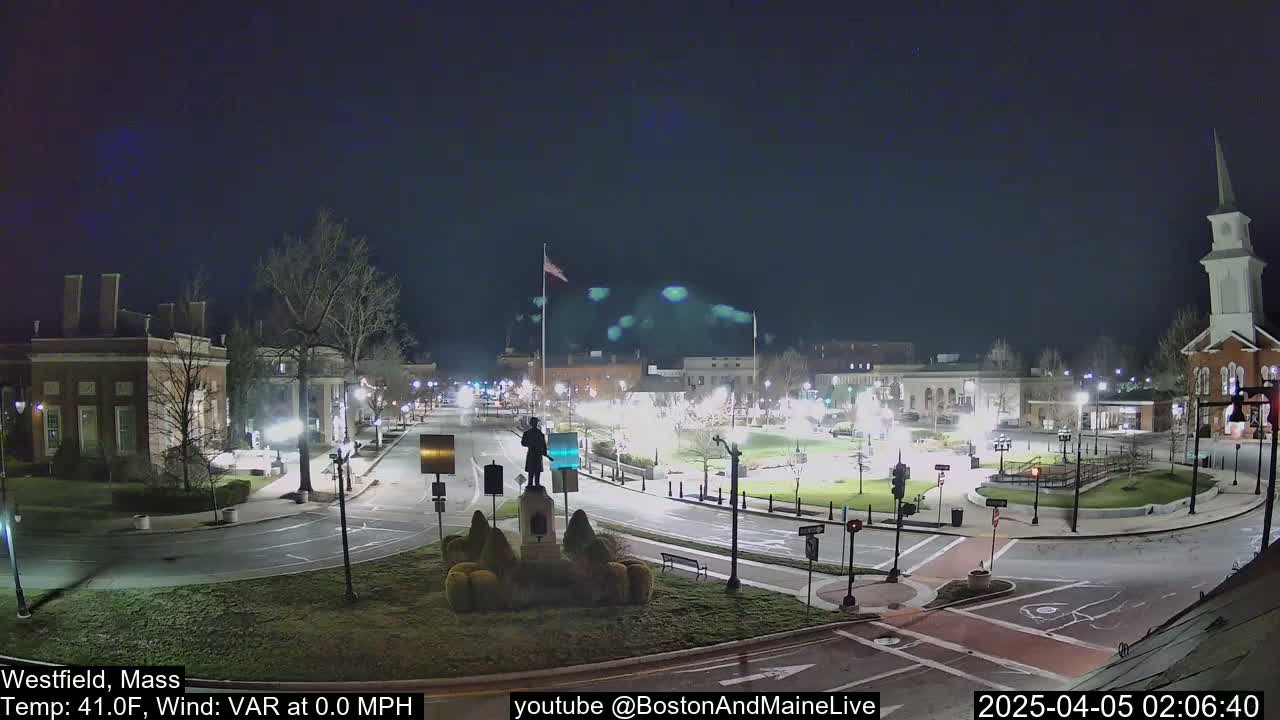 A nighttime view of a town square with a statue in the center, calm weather conditions, and minimal traffic.