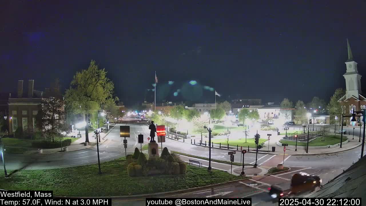 A nighttime view of a town square with a statue in the center, under a clear, dark sky with a 3 mph north wind and a temperature of 57°F.