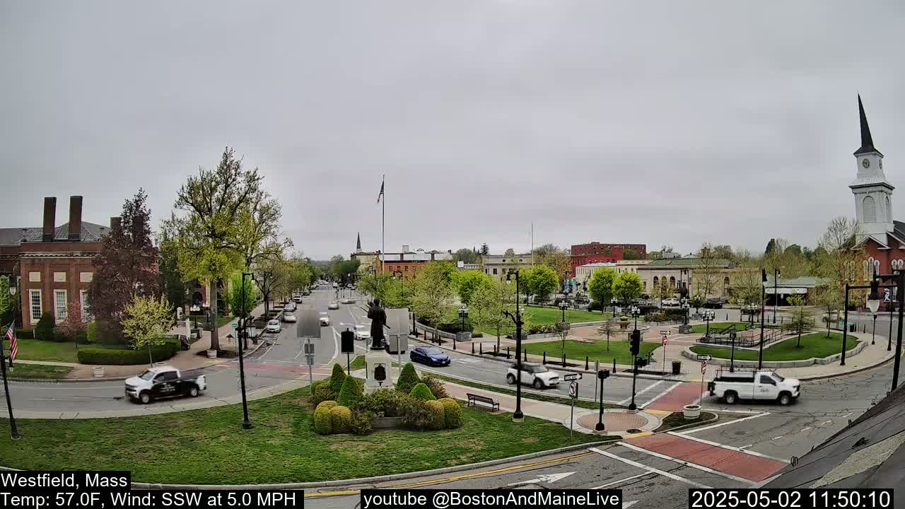 A town square with a statue and a church steeple in the background, under an overcast sky.