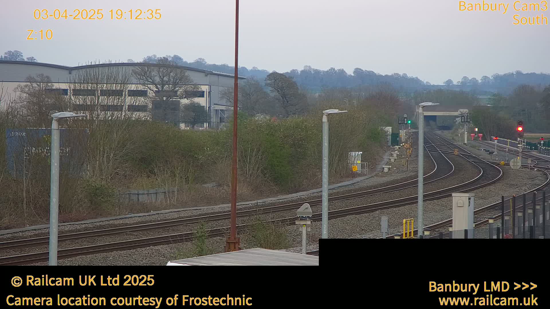 A view of several train tracks curving away from the camera, past a building and some trees, under an overcast sky.