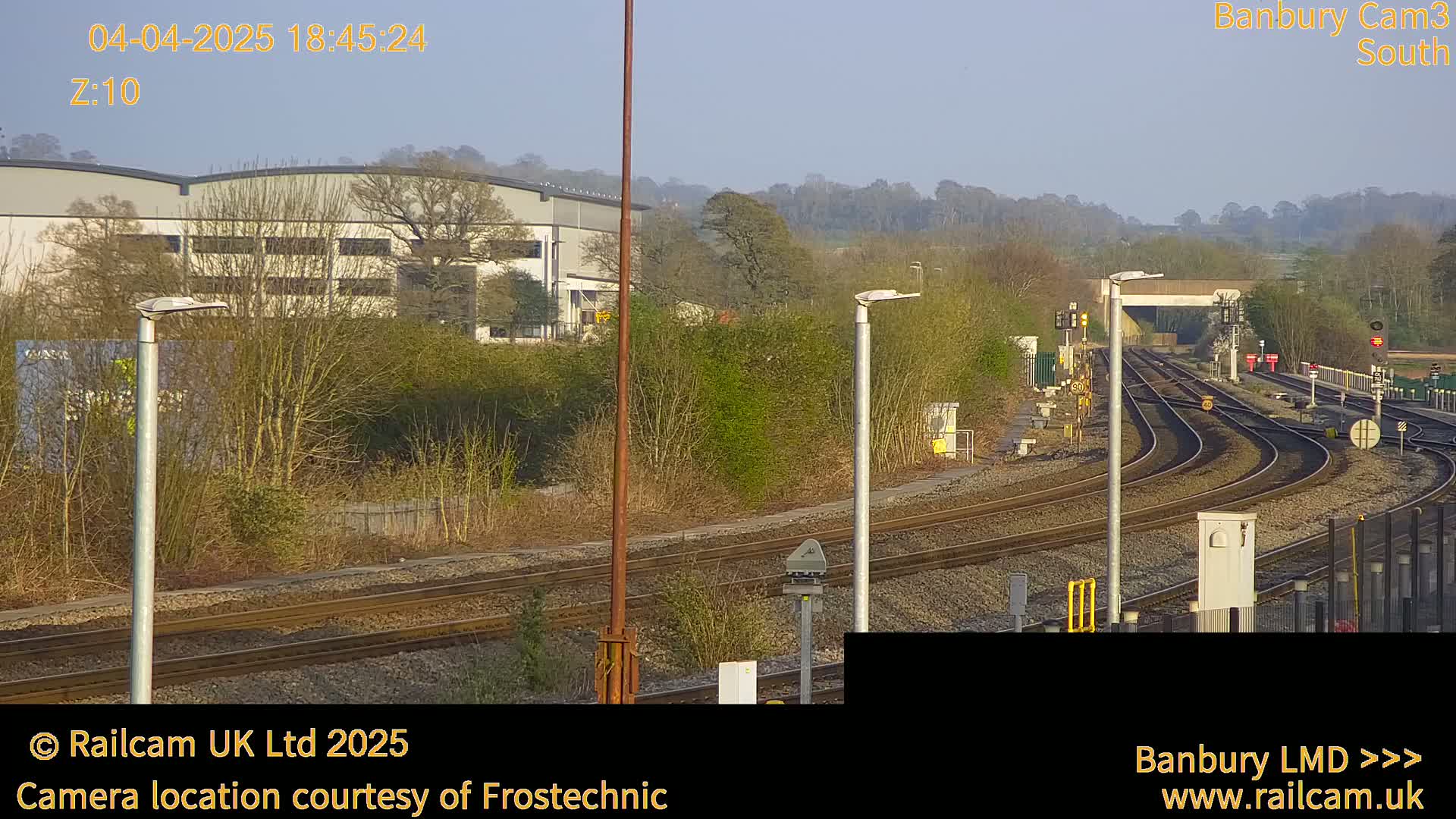 A view of train tracks curving away from the camera, under a clear, bright sky, with buildings and trees in the background.