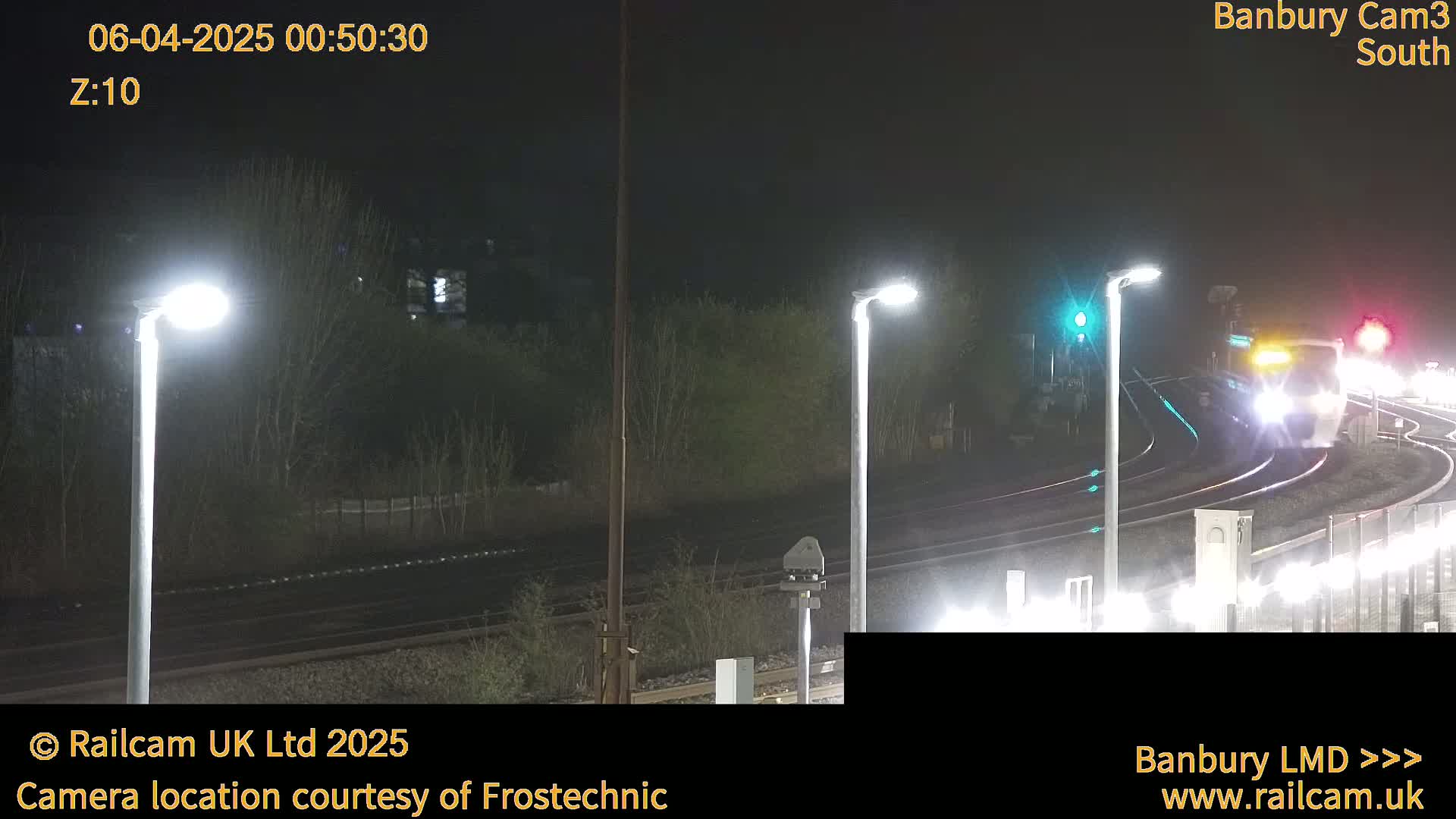At night, a train passes by a railway station illuminated by bright lights.
