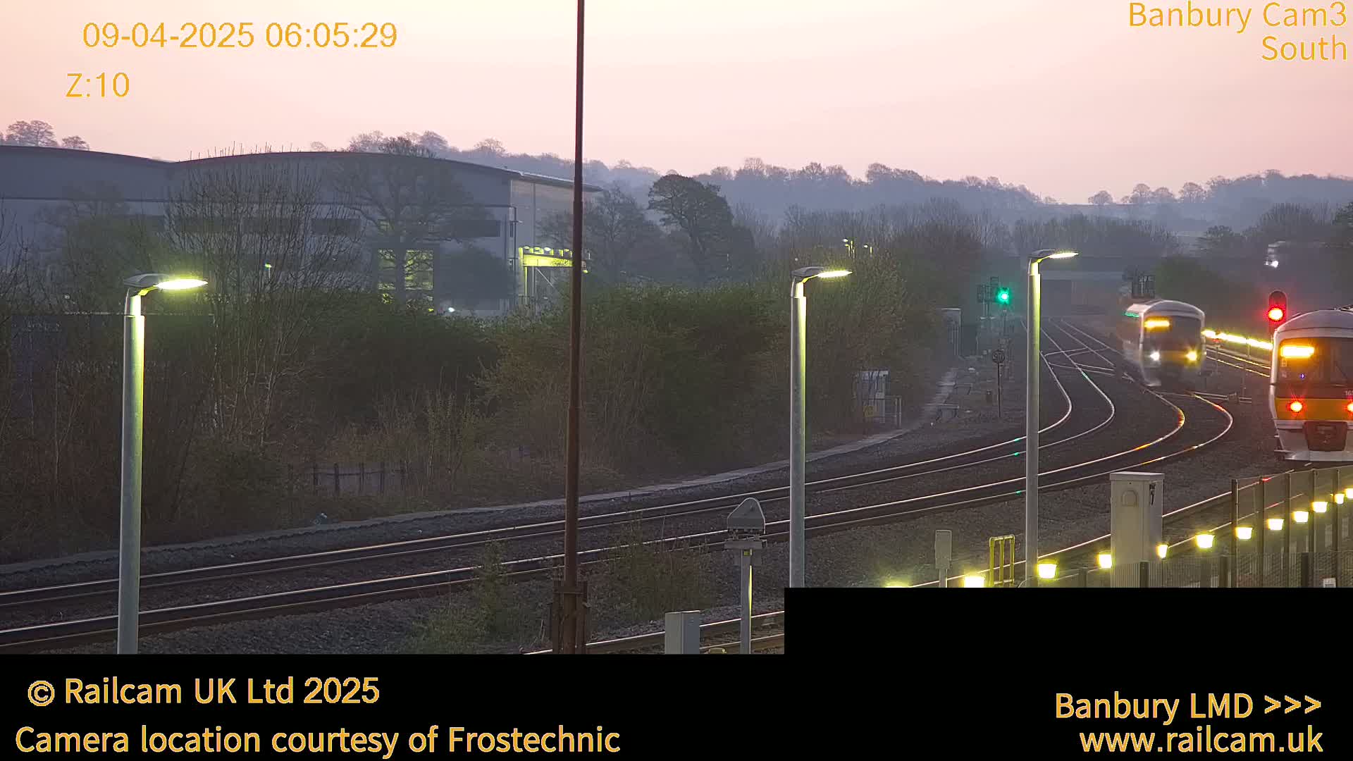 Two trains pass each other on a set of railway tracks at dawn under a hazy pink sky.