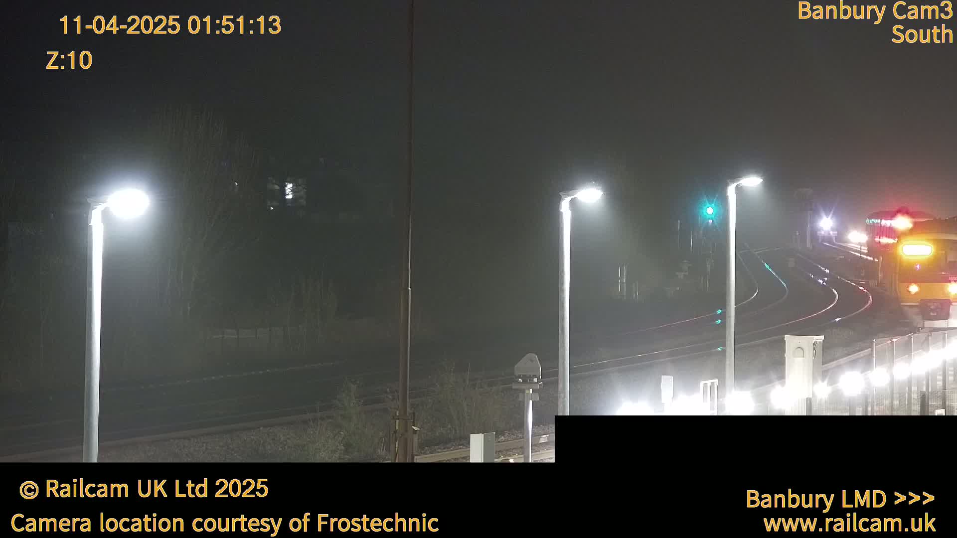 A nighttime, foggy view of a train approaching a station, illuminated by several streetlights.