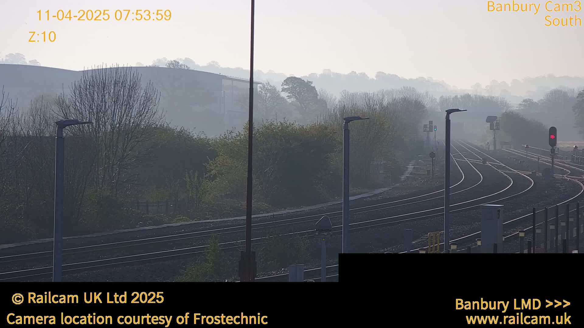 A misty scene shows a railway yard with multiple curving tracks, lamp posts, and low-lying hills in the background.