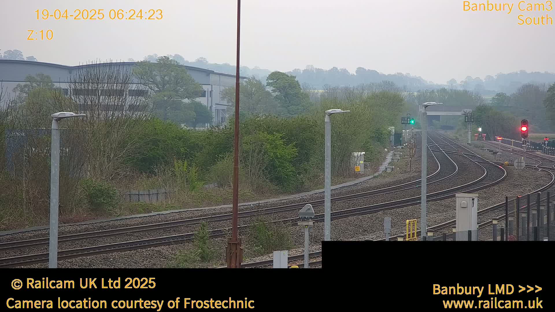 A hazy overcast day reveals a railway yard with multiple tracks curving through a landscape of trees and industrial buildings.