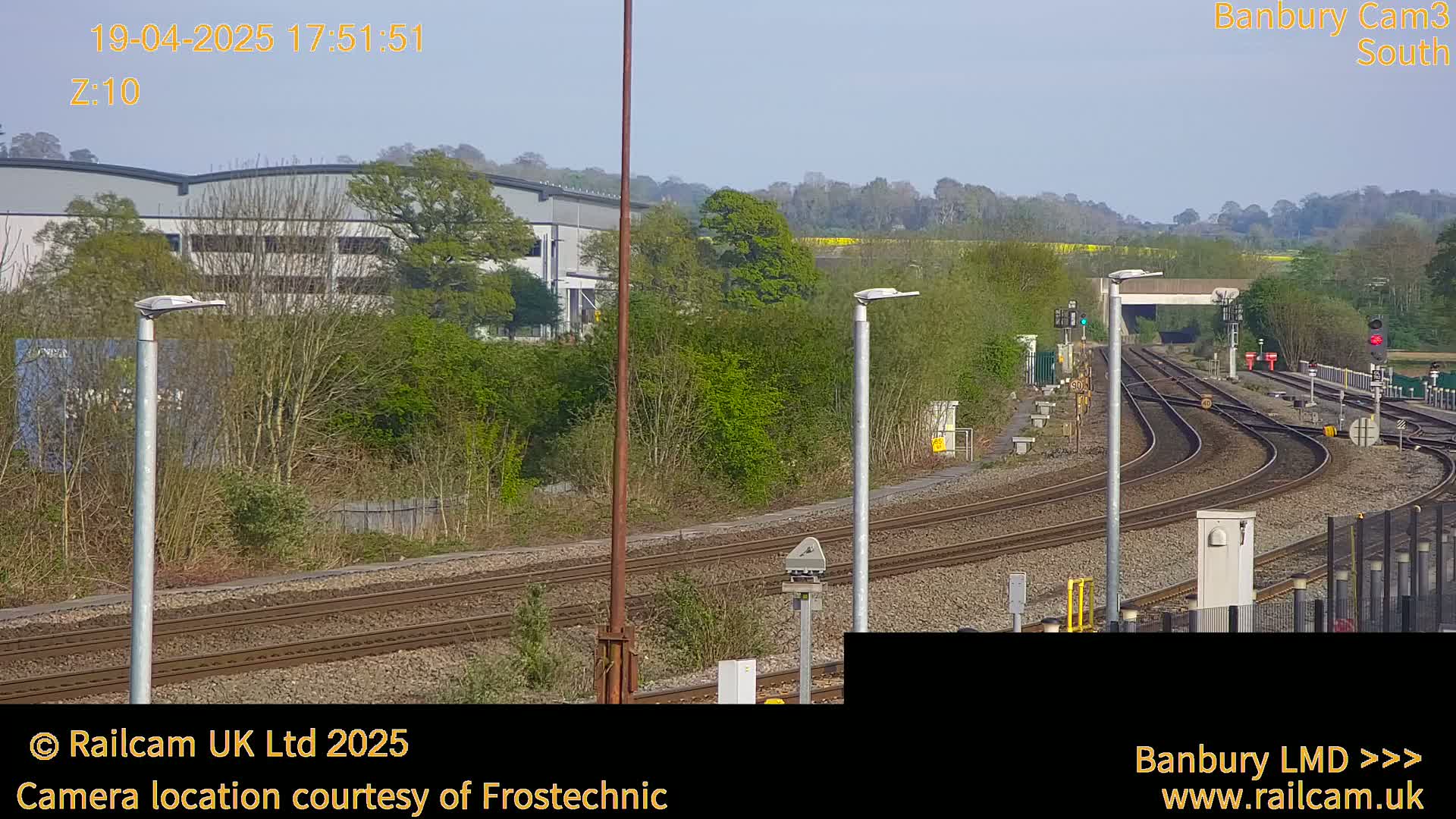 A view of railroad tracks curving through a landscape of green trees and buildings under a clear sky.