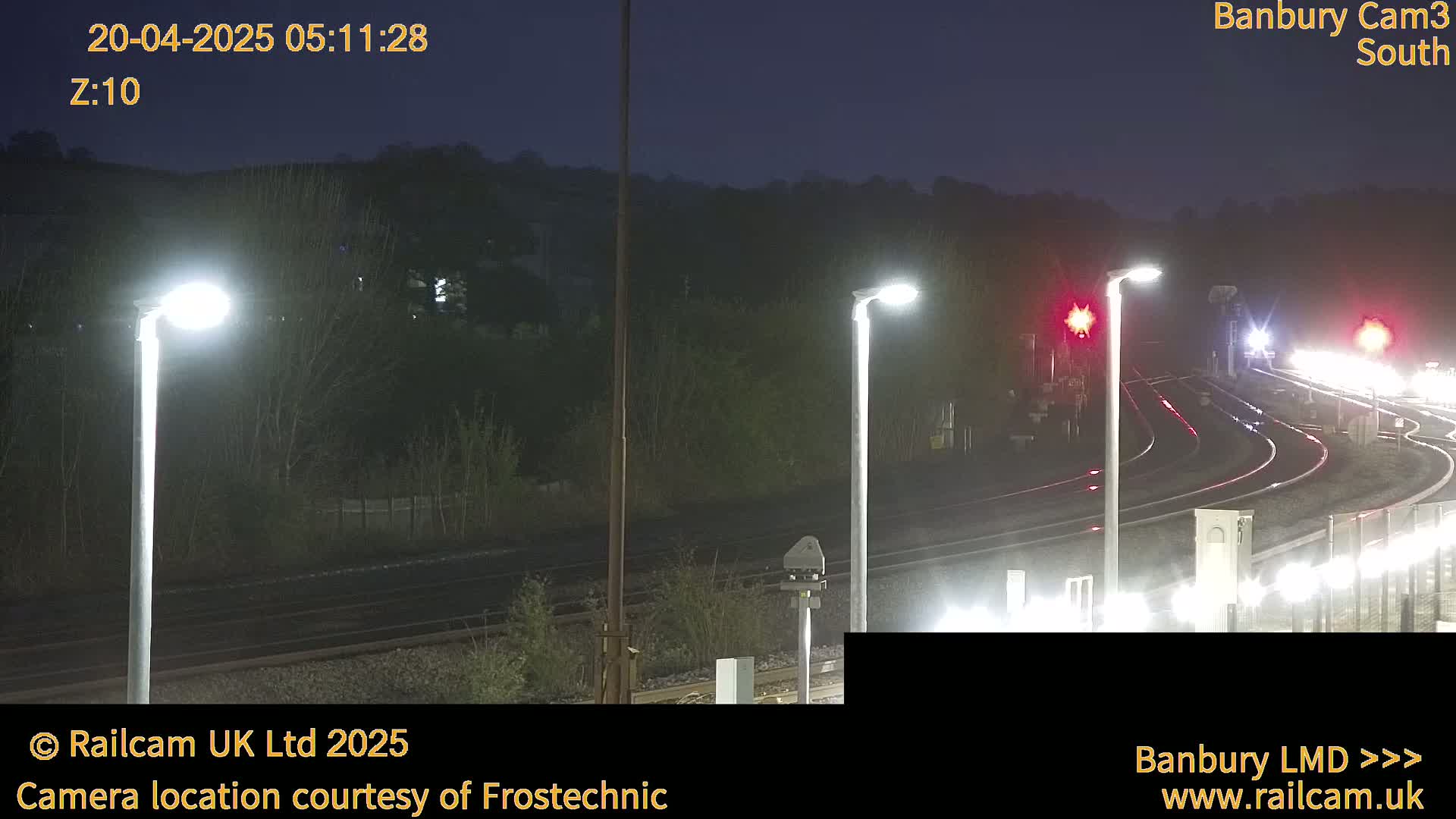 A nighttime view of a train track with several illuminated light poles, under a dark sky.