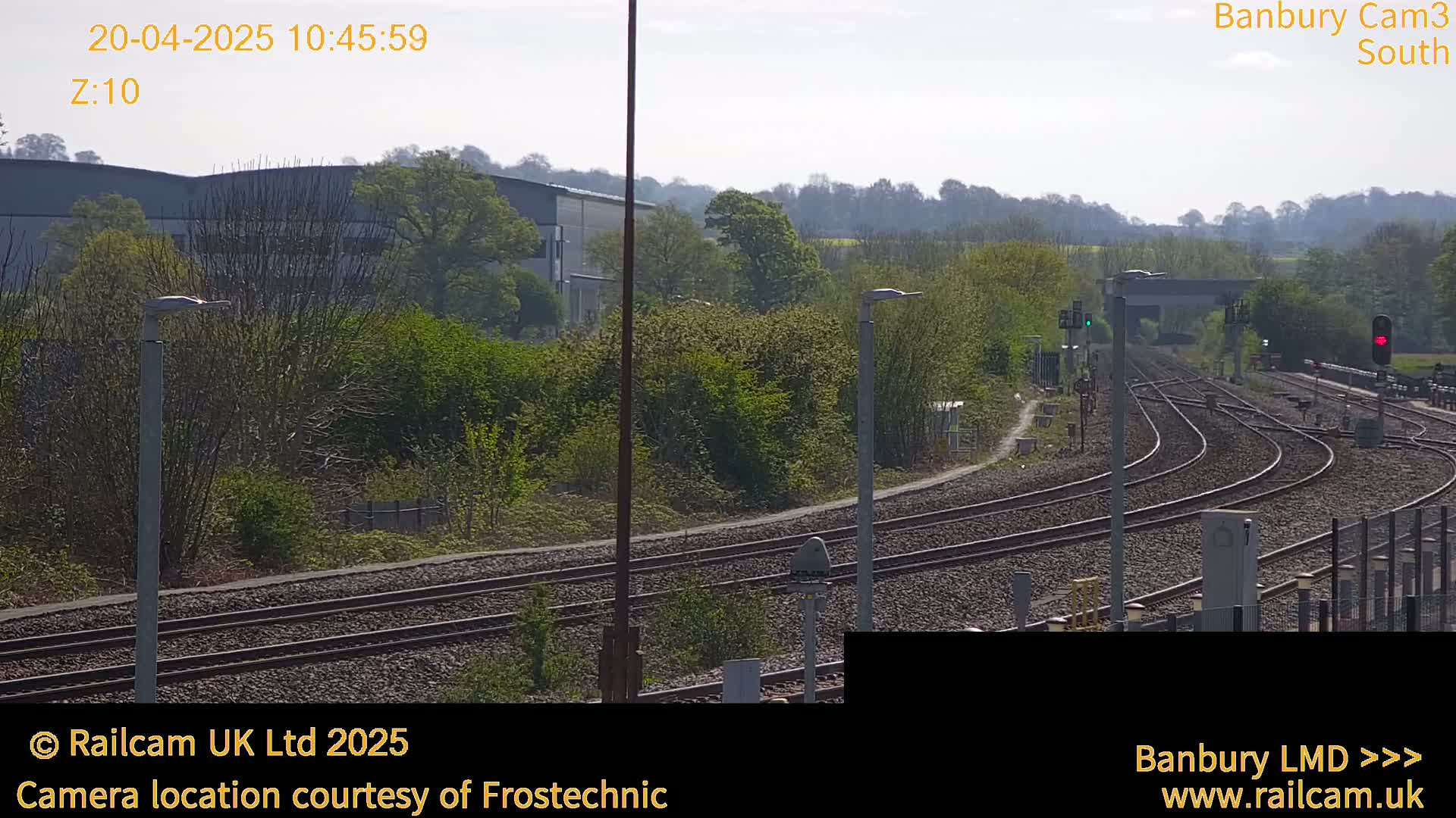 A sunny view of a railway track curving through a landscape of trees and industrial buildings.