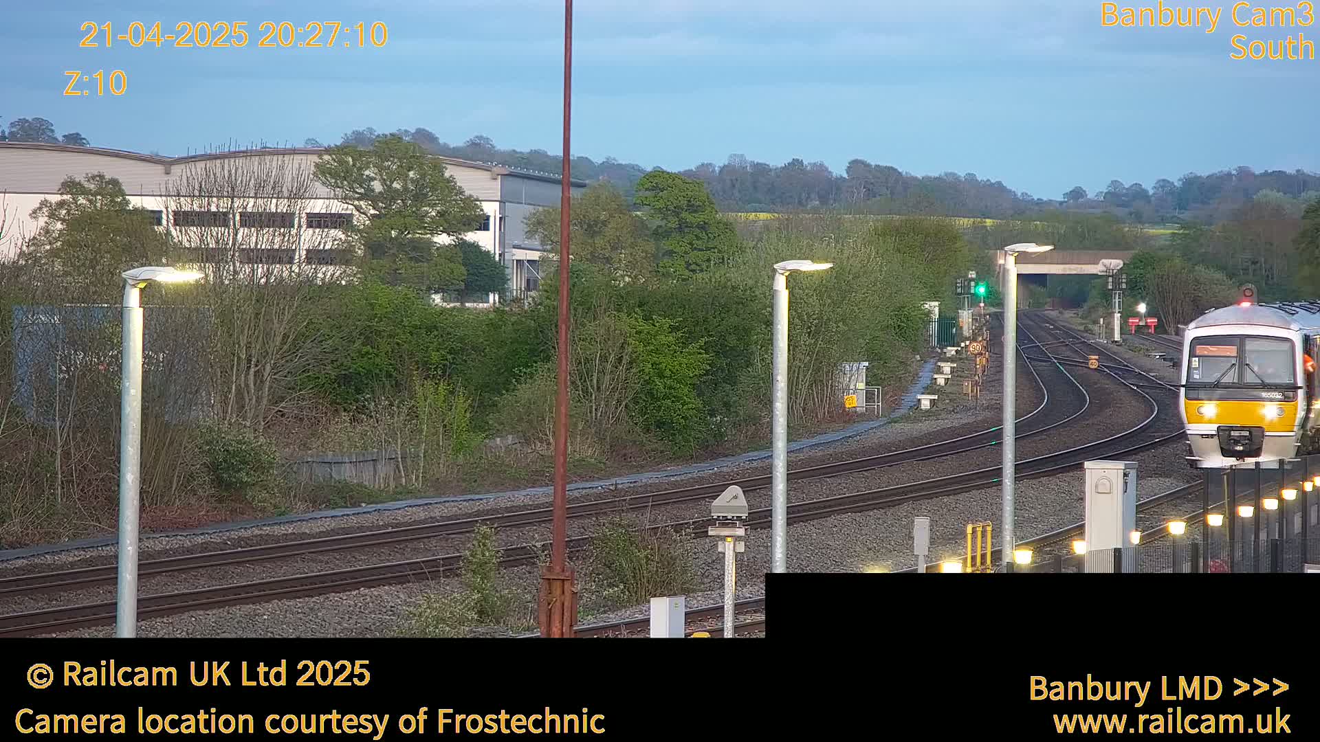 A train approaches a railway station at dusk under a clear sky.