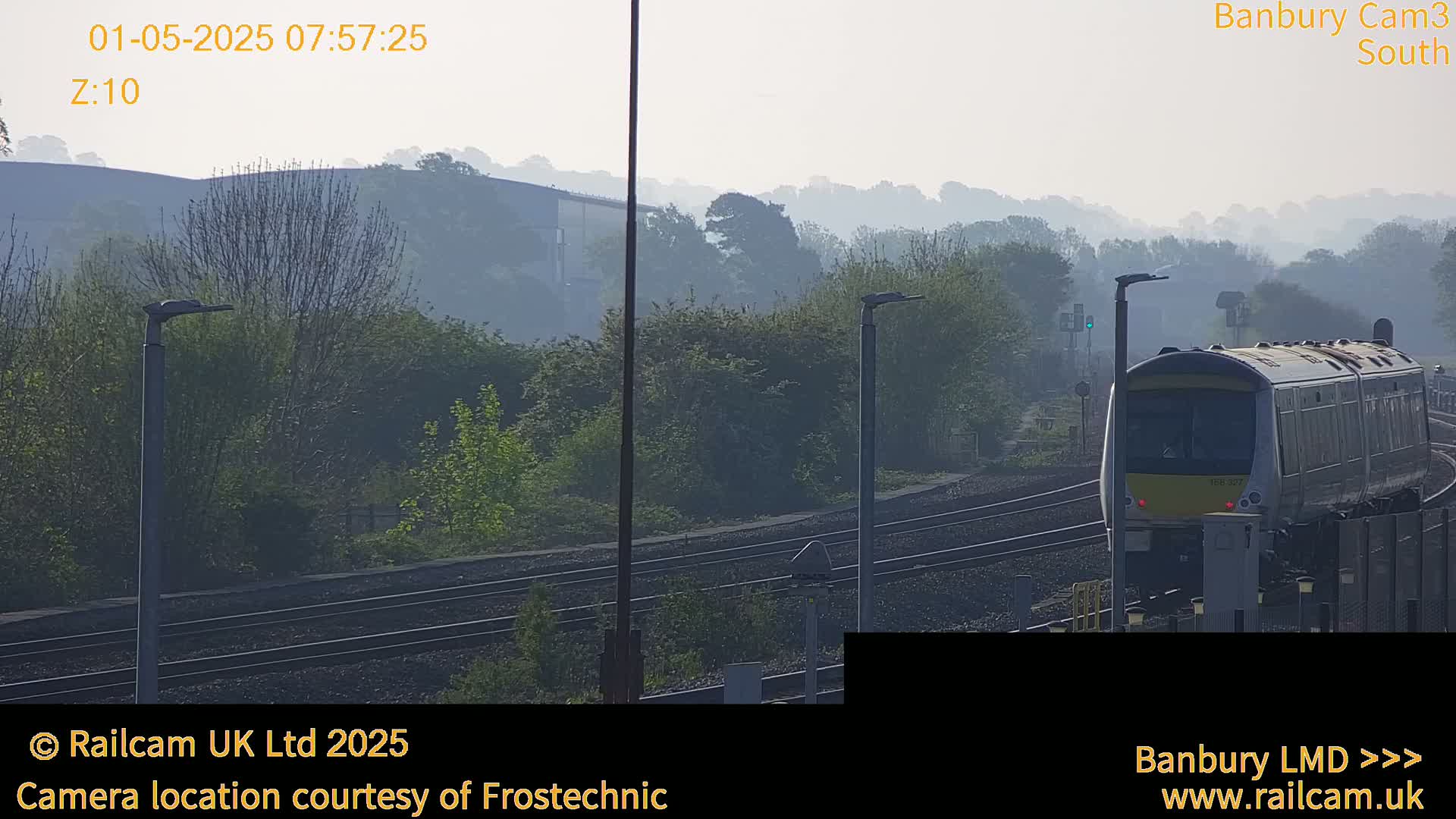 A train approaches on a railway track, surrounded by hazy, tree-covered hills in the early morning.
