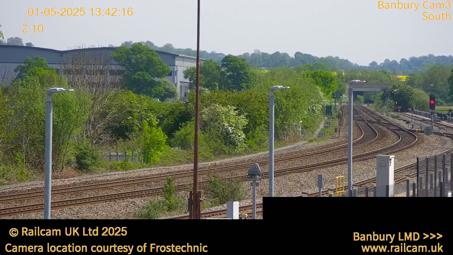 A sunny view of curving train tracks surrounded by green trees and a building in the background.