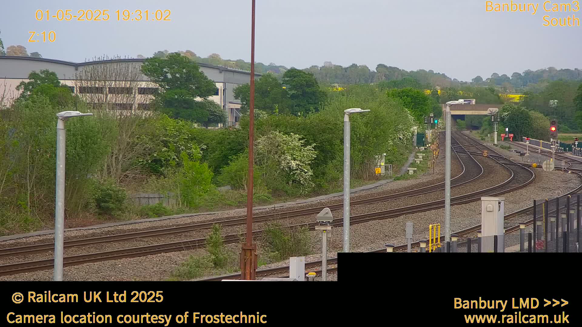 Several sets of train tracks curve through a landscape of green trees and shrubs under an overcast sky.