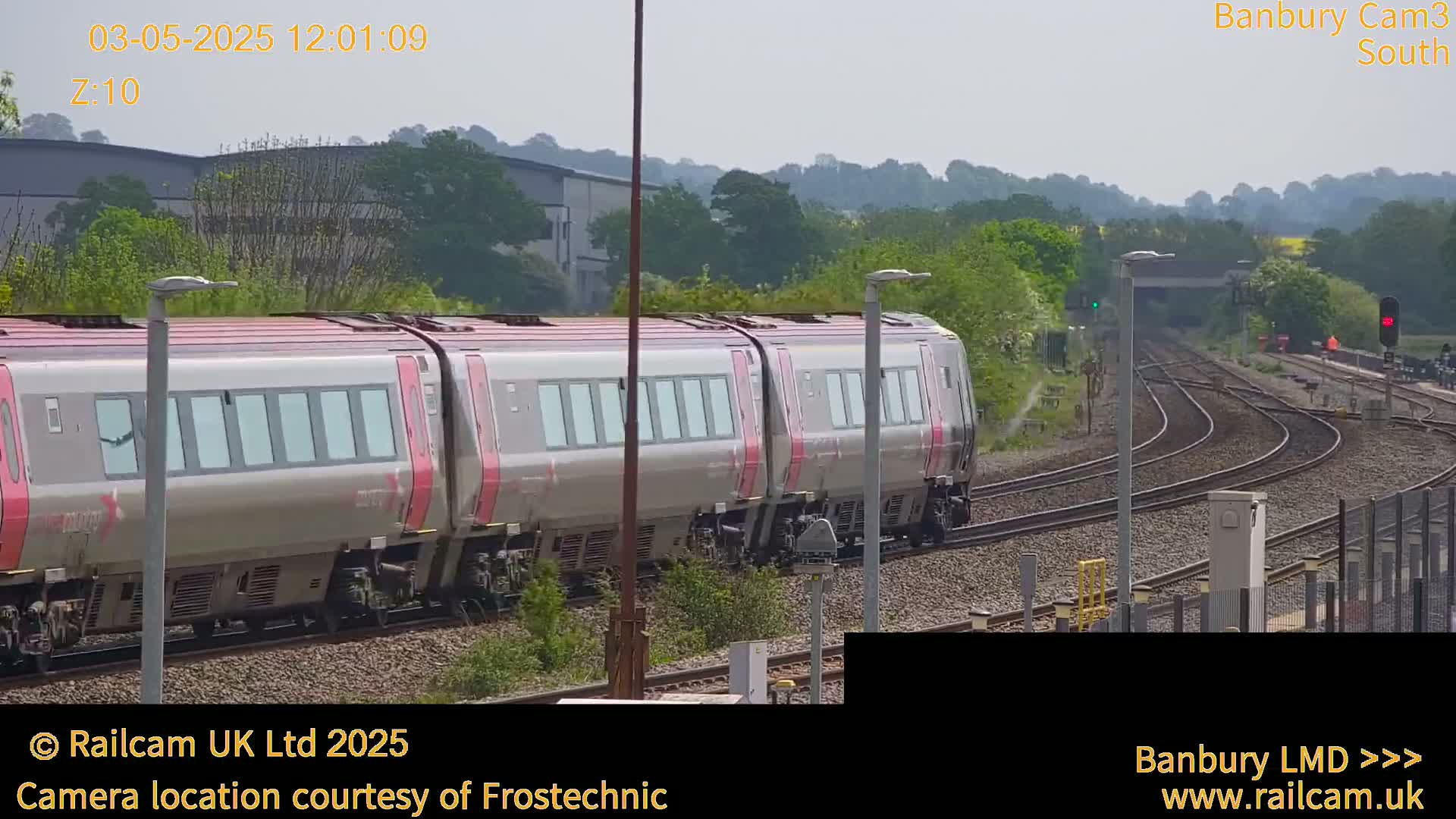 A long, silver and maroon train passes by on a sunny day.