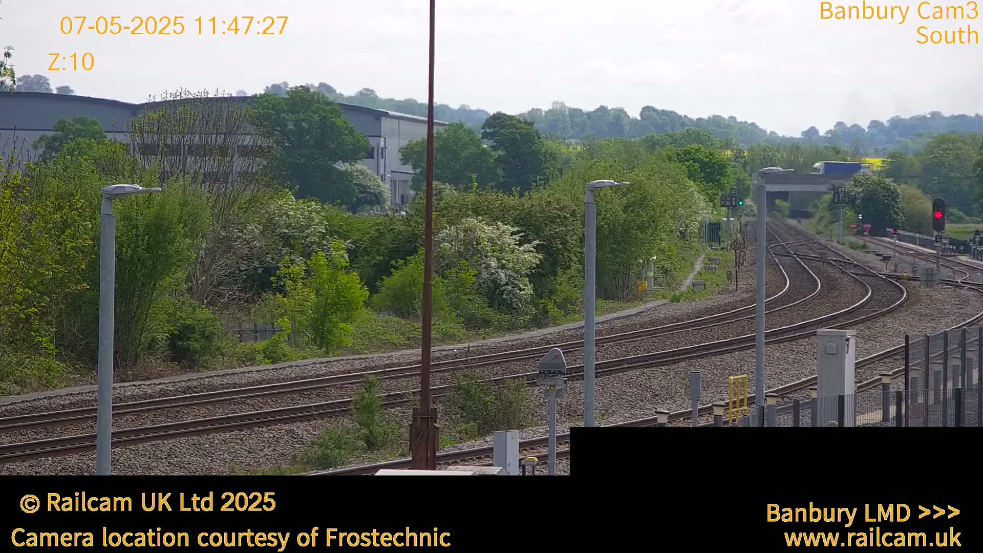 A view of railway tracks curving through a landscape of lush green trees and bushes under a partly cloudy sky.
