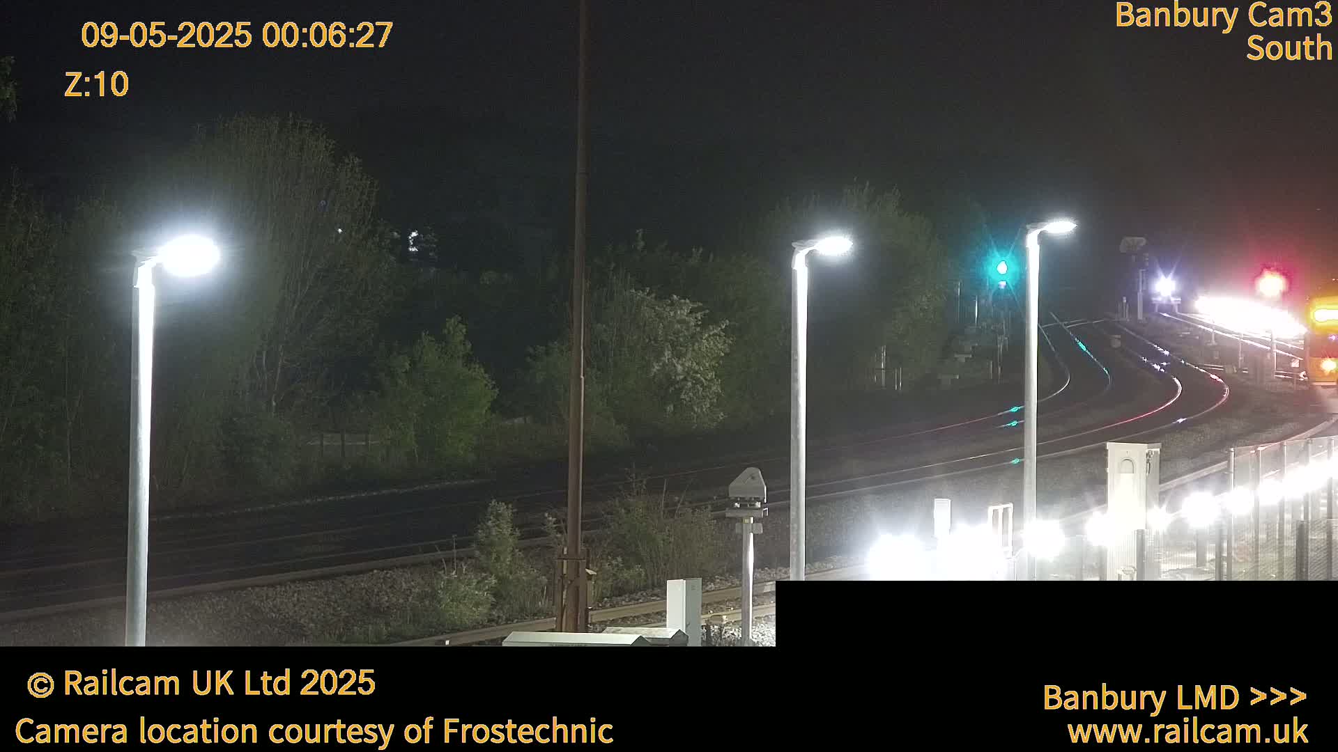 A nighttime view of a train track with several lights illuminating the scene and dark green vegetation.