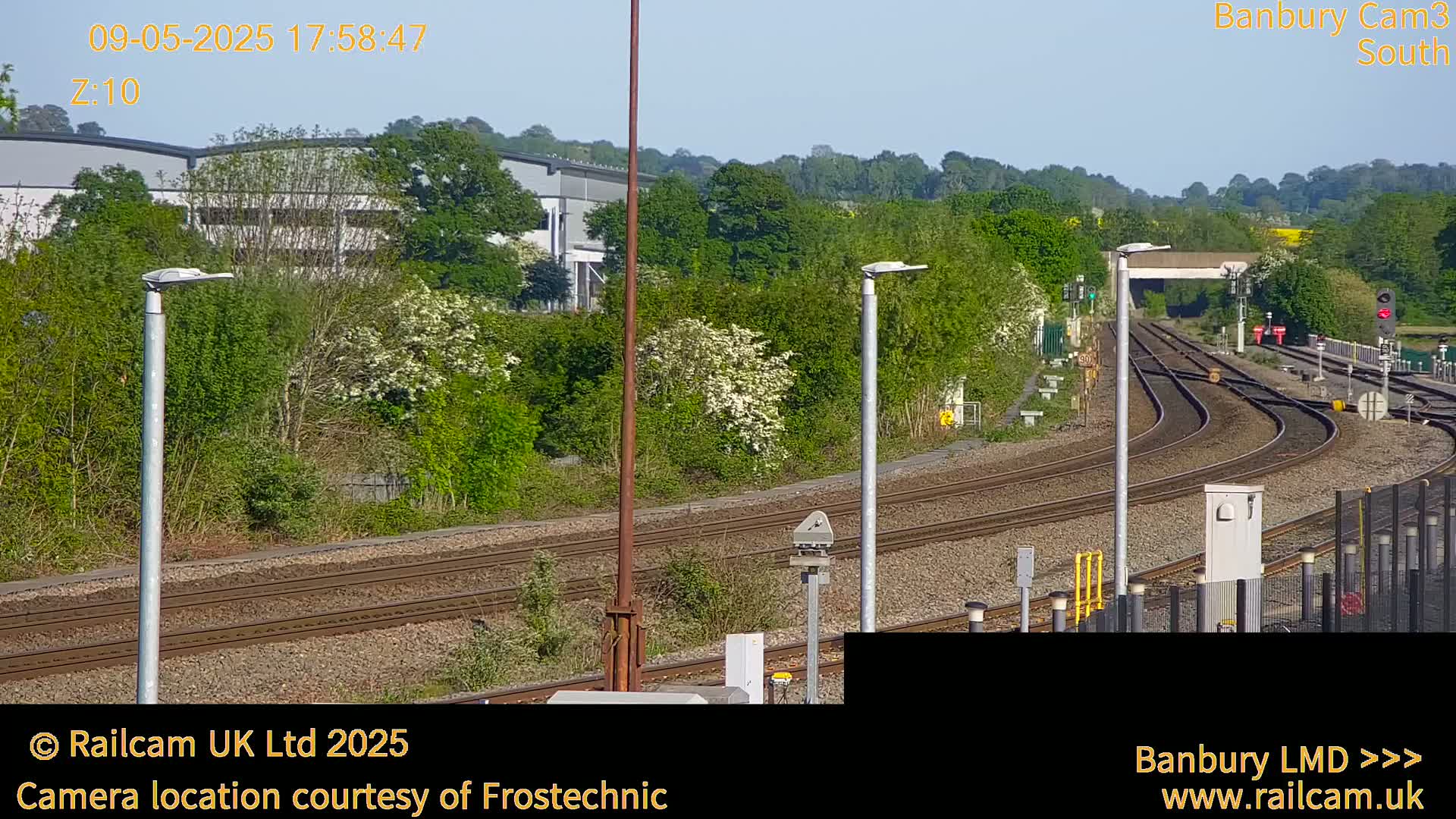A sunny view of several train tracks curving through a landscape of green vegetation and industrial buildings.