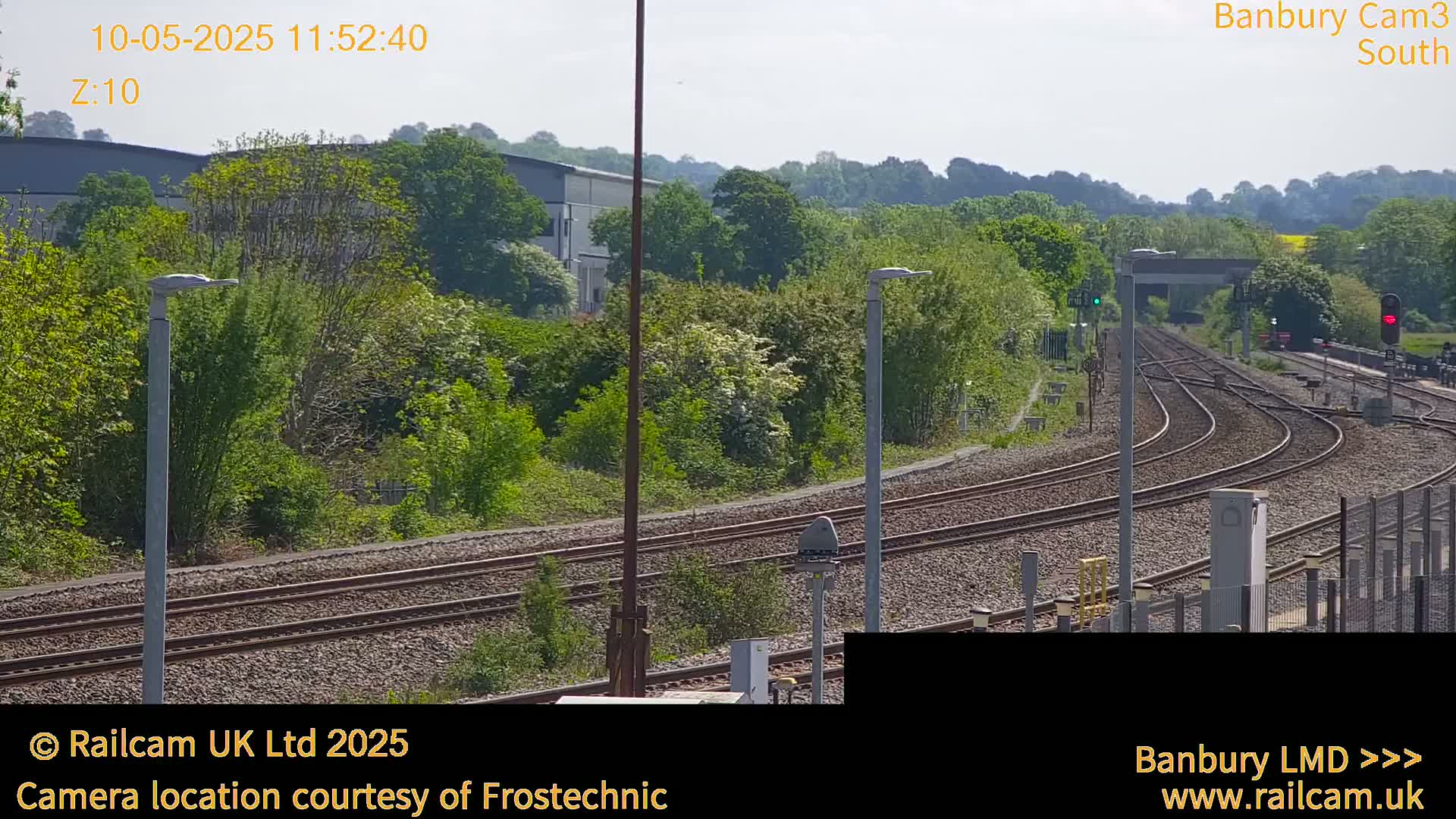 A sunny view of multiple train tracks curving through a green landscape with trees and a building in the distance.