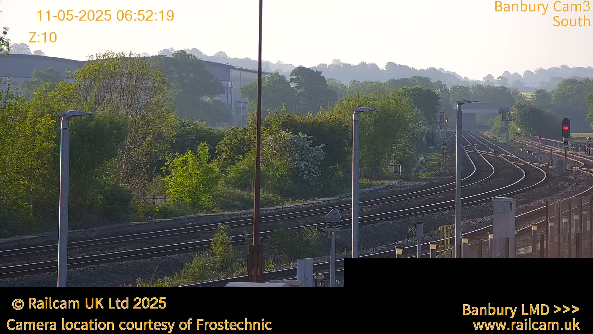 Several sets of train tracks curve through a landscape of green trees and hazy morning light.