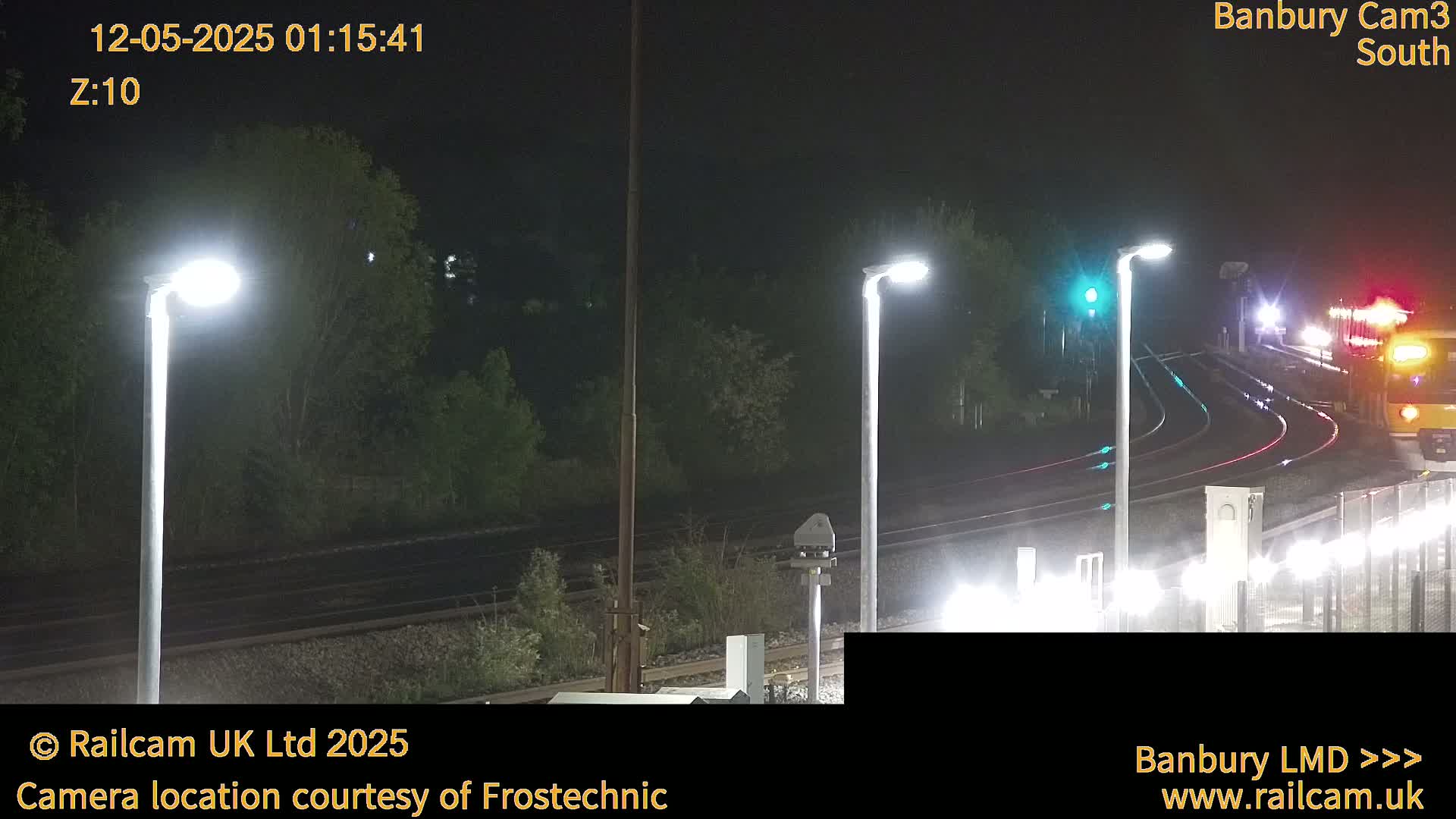 A nighttime view of a train passing through a station illuminated by bright lights.