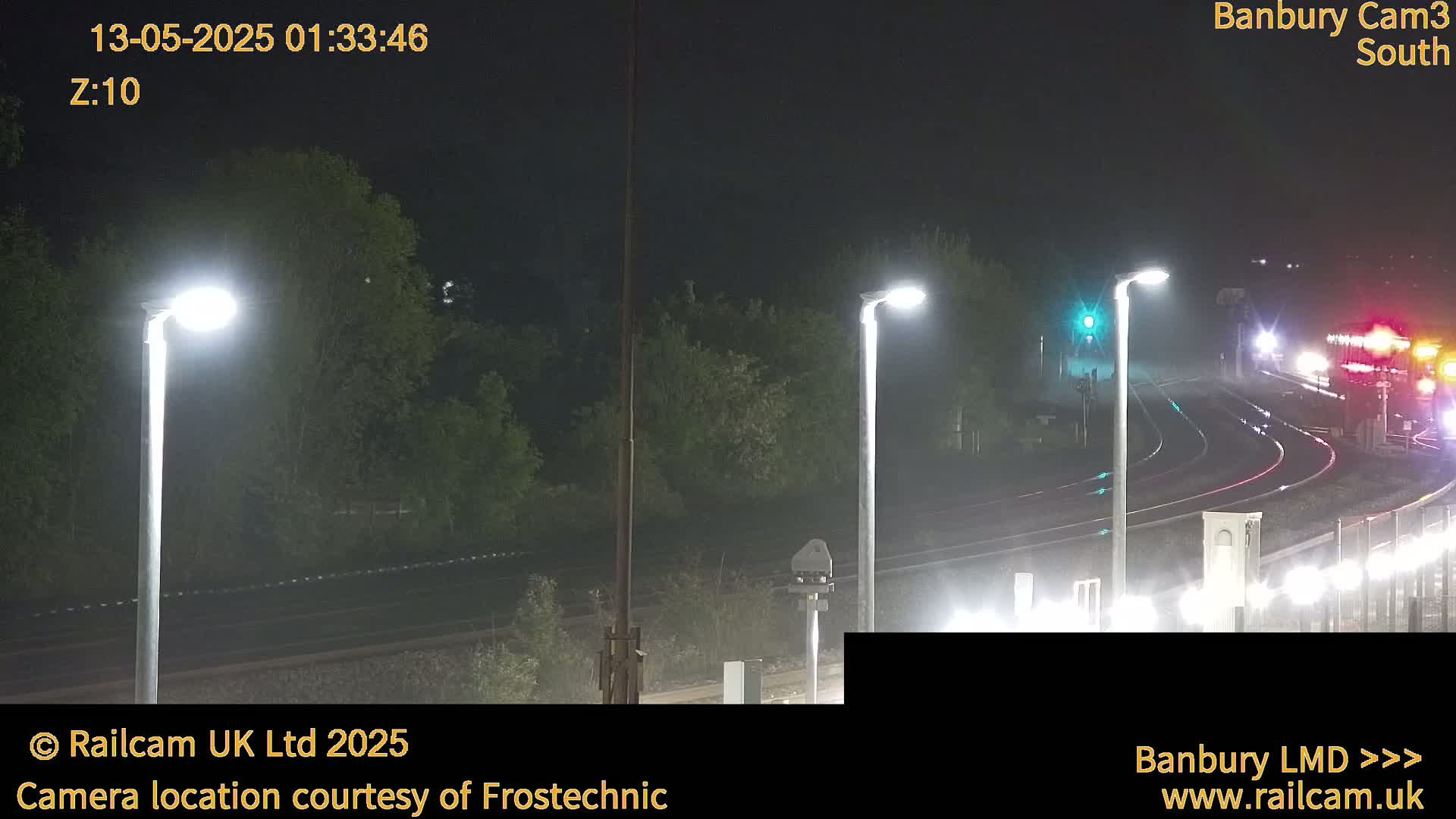 A nighttime view of a train passing through a station under hazy conditions, illuminated by several bright streetlights.