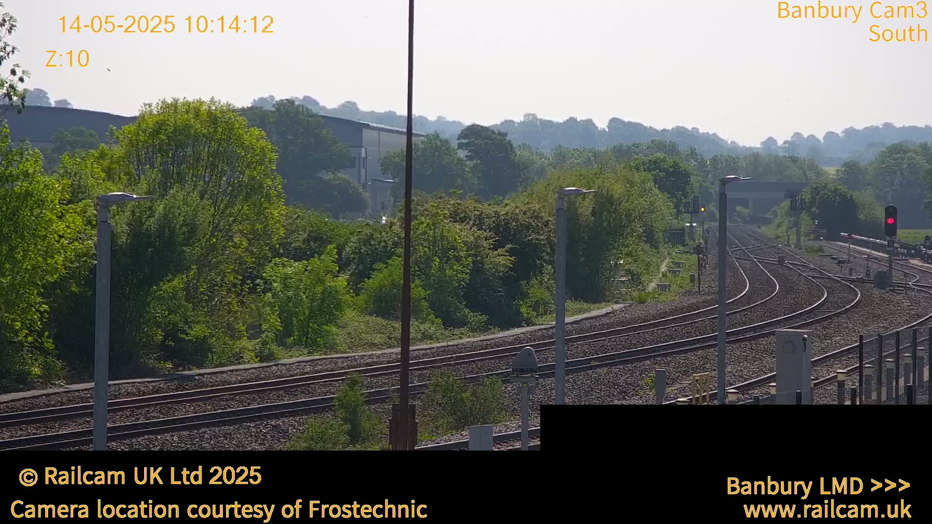 A sunny view of a railway track branching off into several directions, surrounded by lush green trees and vegetation.