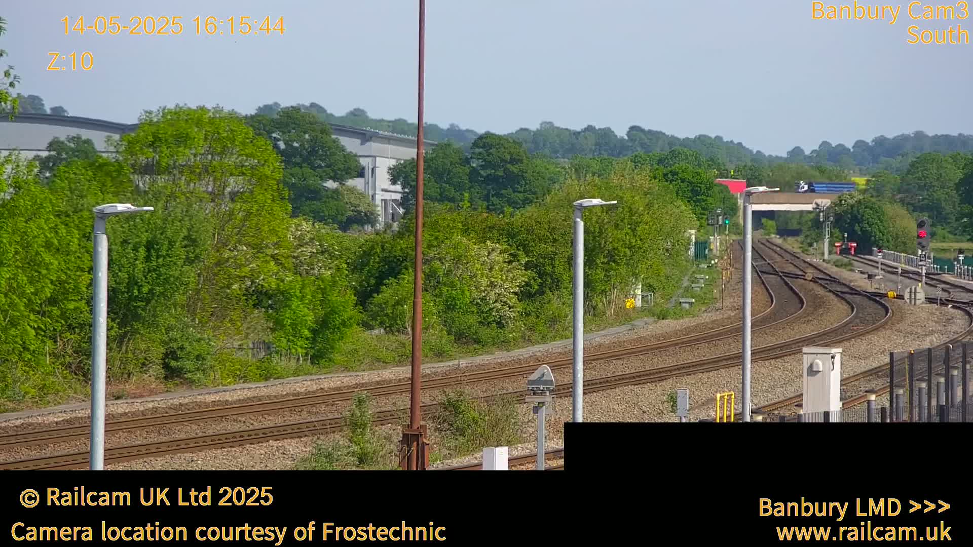 A sunny view of a railway track branching off into several directions, surrounded by green trees and bushes under a clear sky.