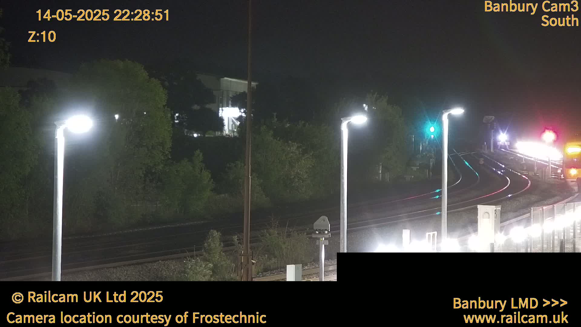 At night, illuminated train tracks curve through a dark landscape under bright lamp posts.