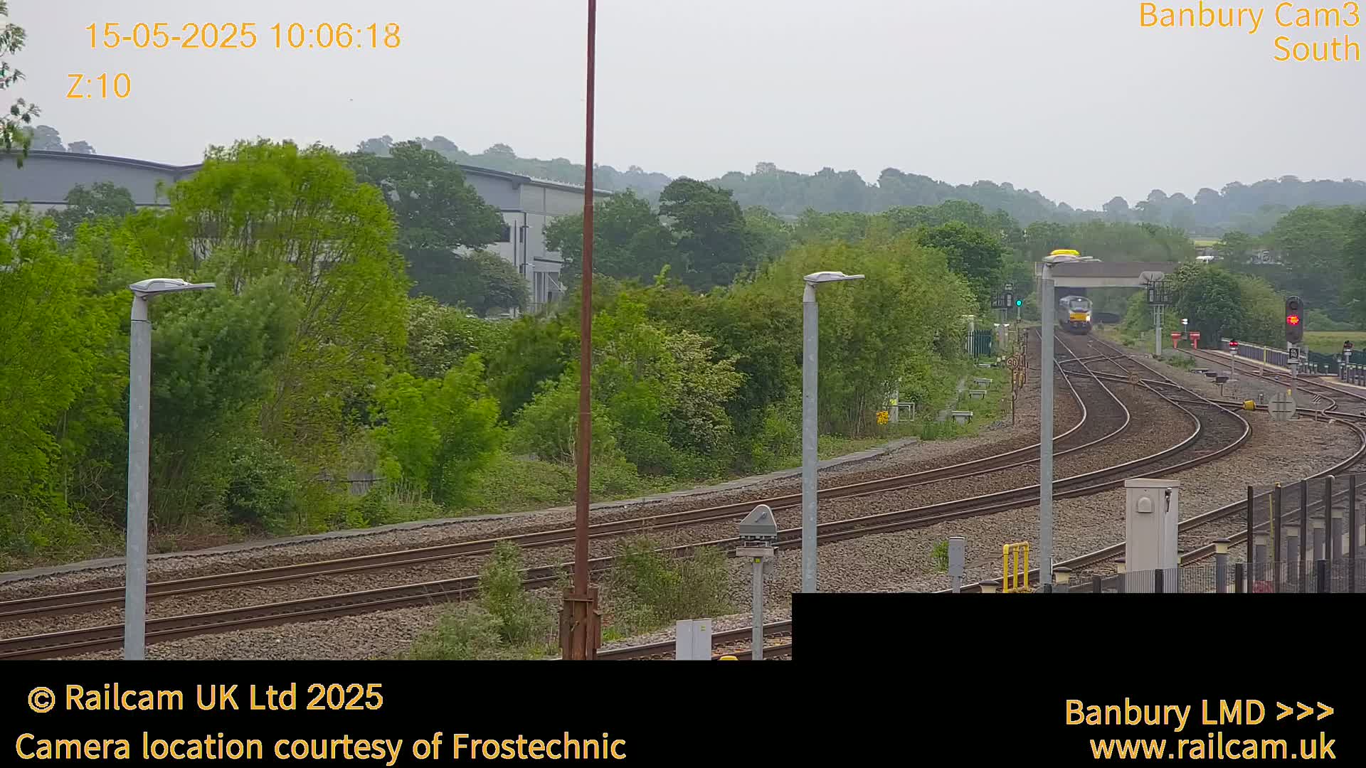 A train is traveling along a railway line through a green, tree-lined landscape under an overcast sky.