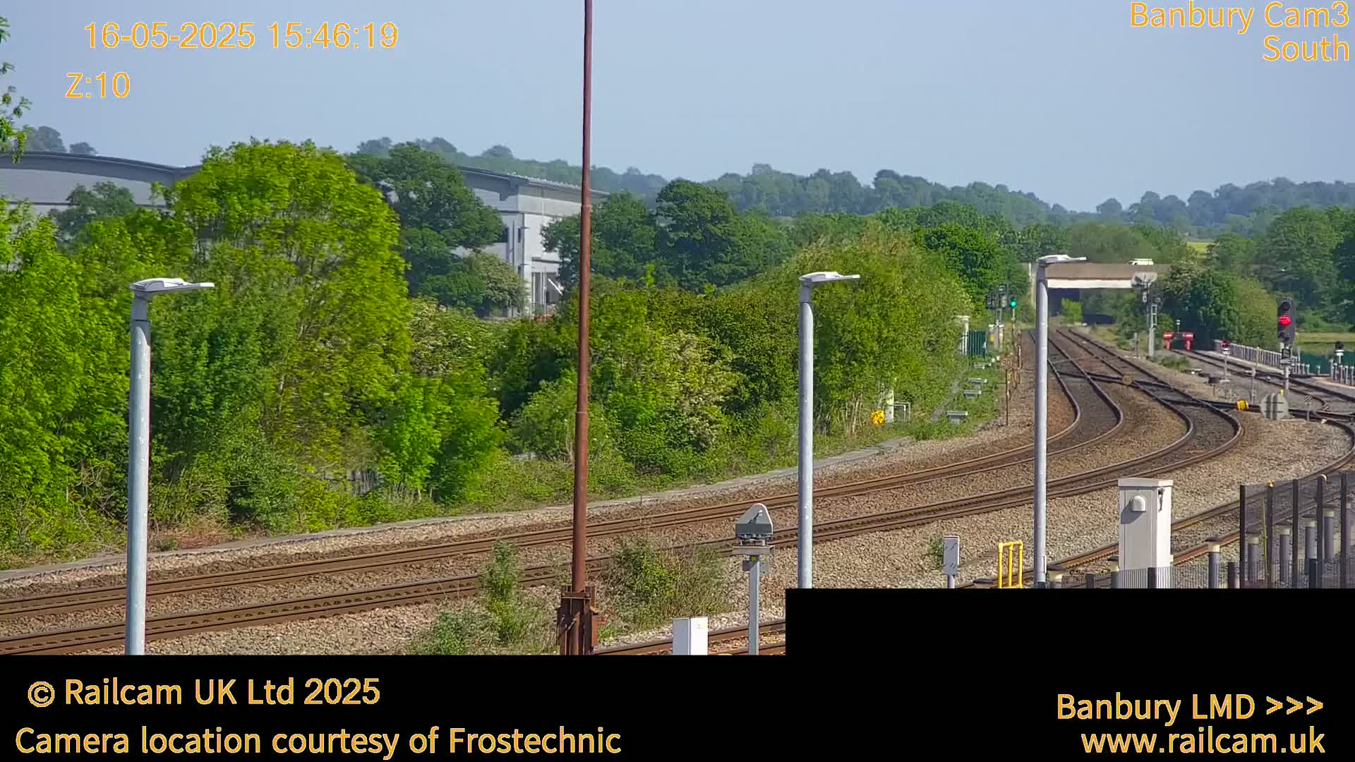 A sunny view of a railway track curving through a landscape of lush green trees and bushes, under a clear sky.
