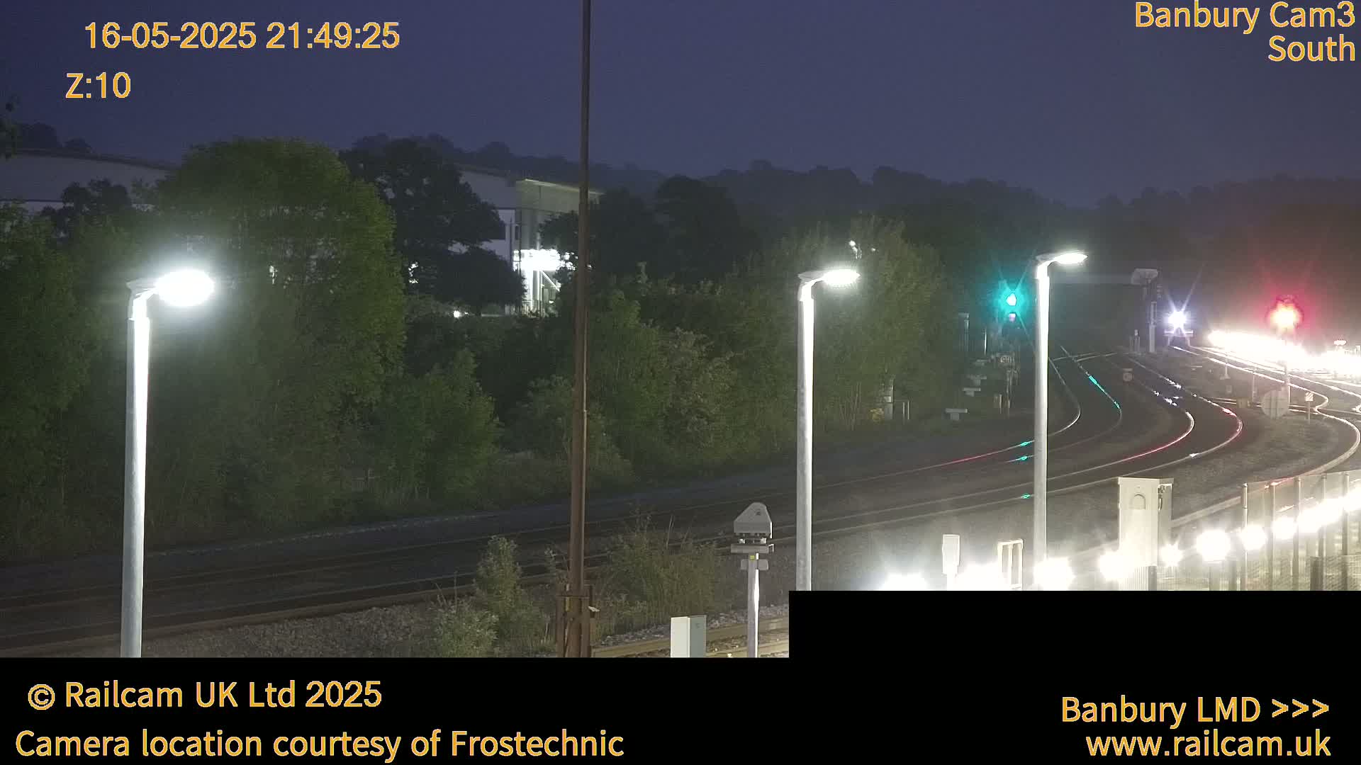 A nighttime view of a railway track curving into the distance, illuminated by several streetlights, under a dark, clear sky.