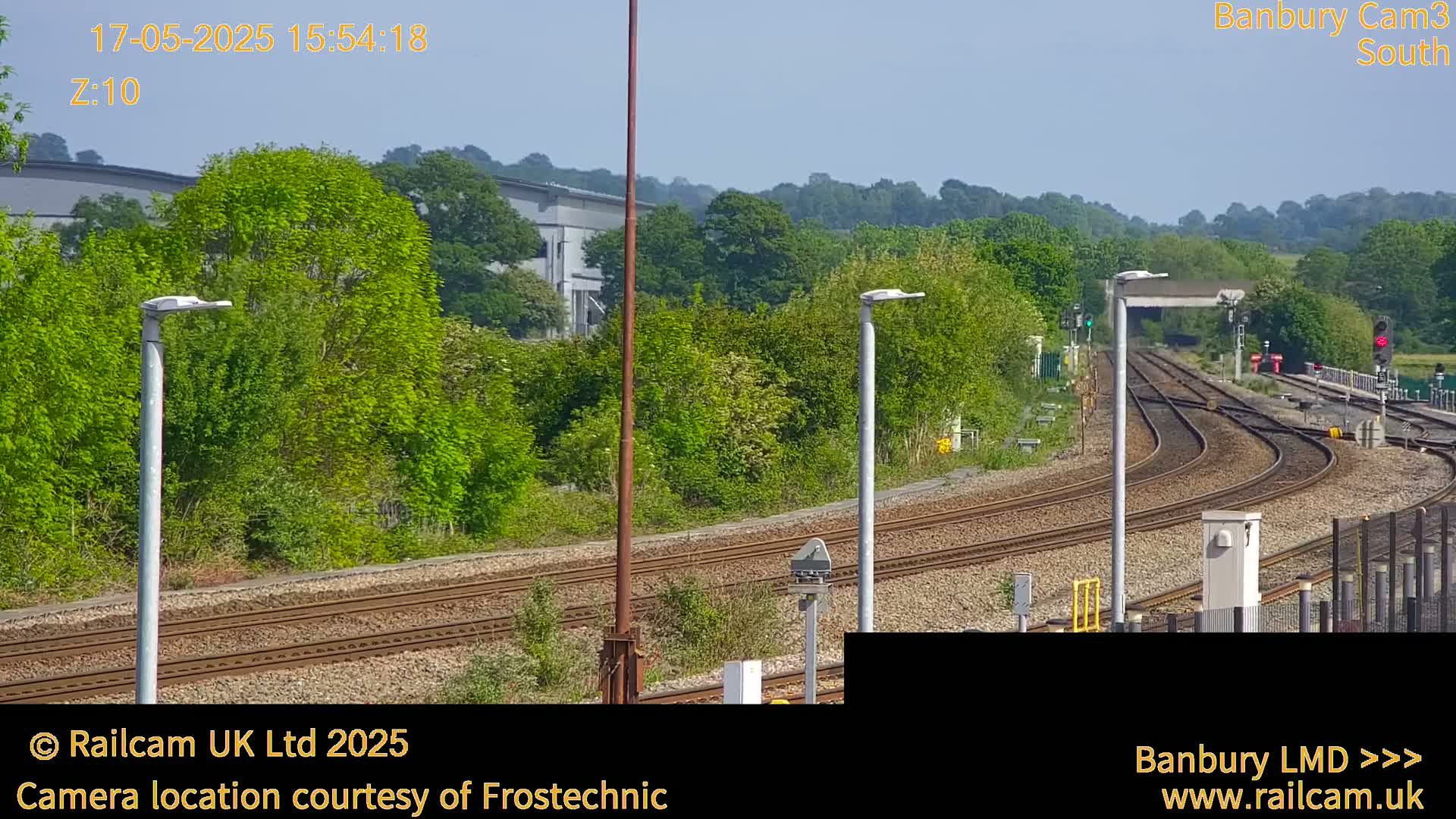 A sunny view of a railway track curving through lush green vegetation, under a clear sky.