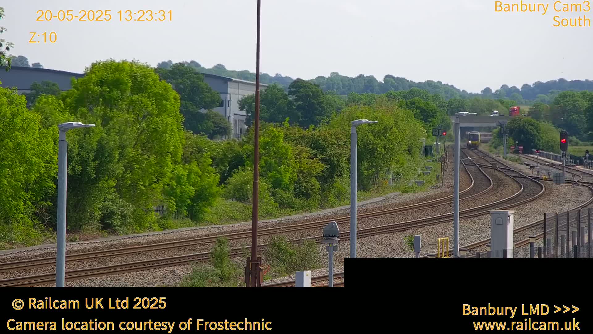 A train travels along a railway track that curves through a lush green landscape under a bright, sunny sky.