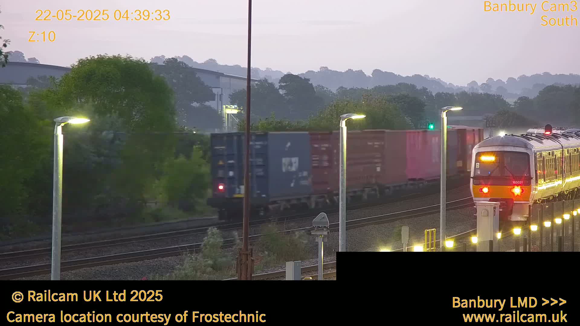 A passenger train passes a freight train on a railway track at dawn under a hazy sky.