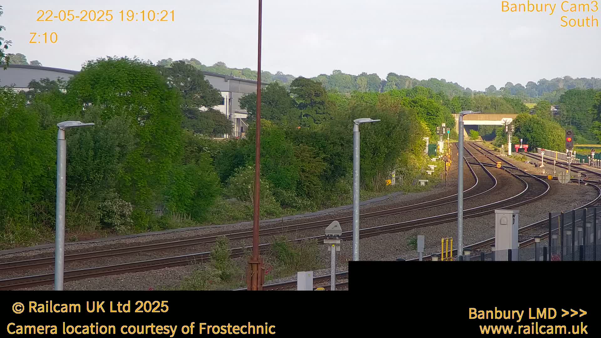 A view of train tracks curving away from the camera under a clear evening sky, surrounded by lush green trees and vegetation.