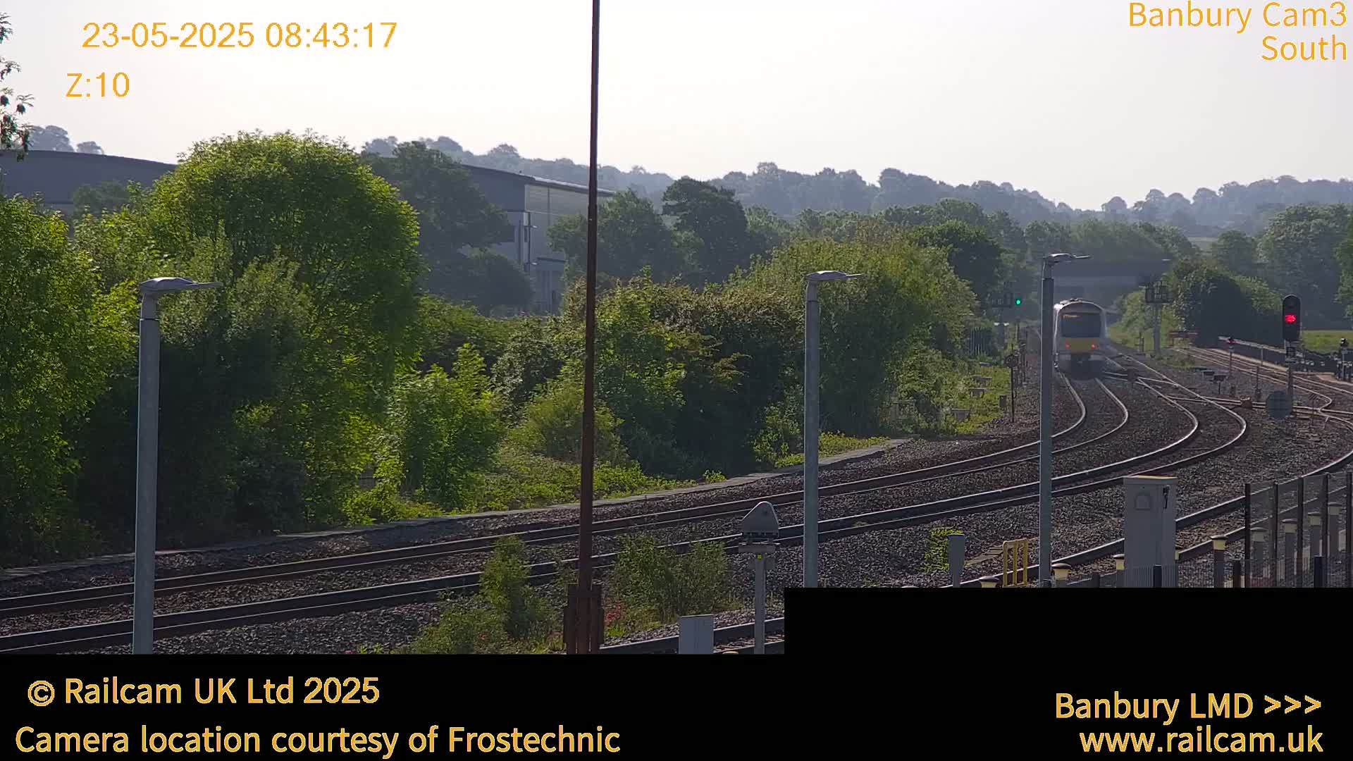 A train is traveling on a railway track surrounded by lush green vegetation under a hazy sky.