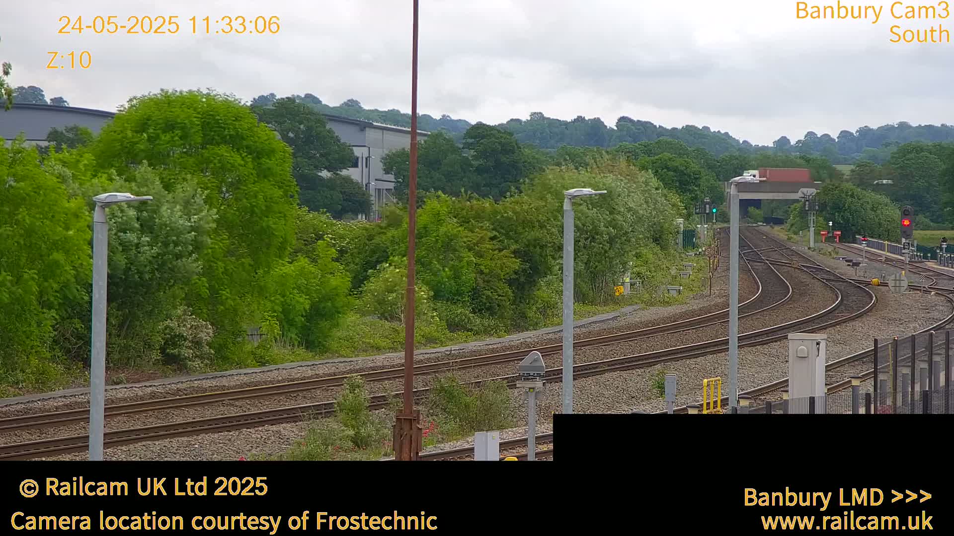 A view of curving railway tracks surrounded by lush green trees and vegetation under an overcast sky.