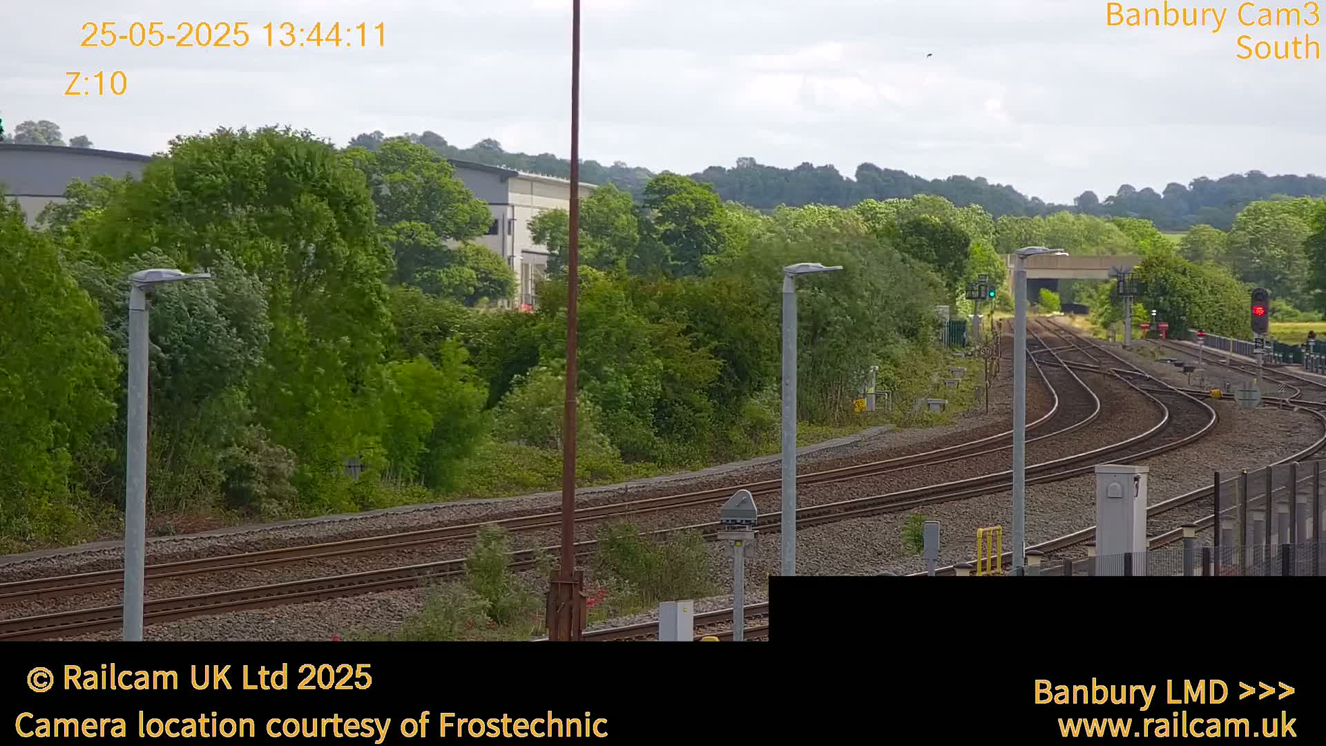 A slightly overcast day shows a view of multiple train tracks curving through a lush green landscape, with buildings and trees in the background.