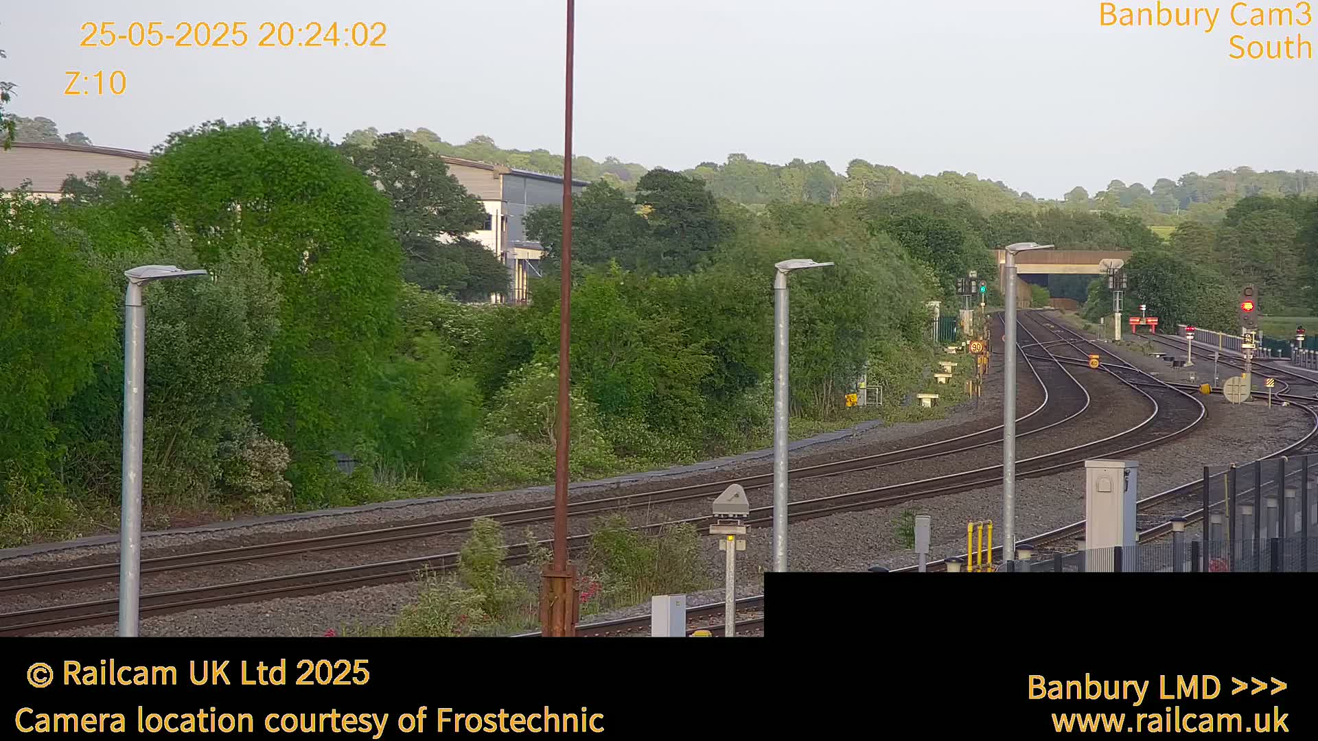 A view of several train tracks curving through a lush green landscape under a partly cloudy evening sky.