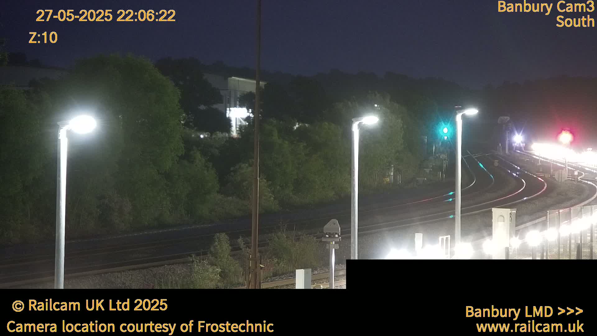 A nighttime view of a train station with several lit lampposts and train tracks curving through the scene.