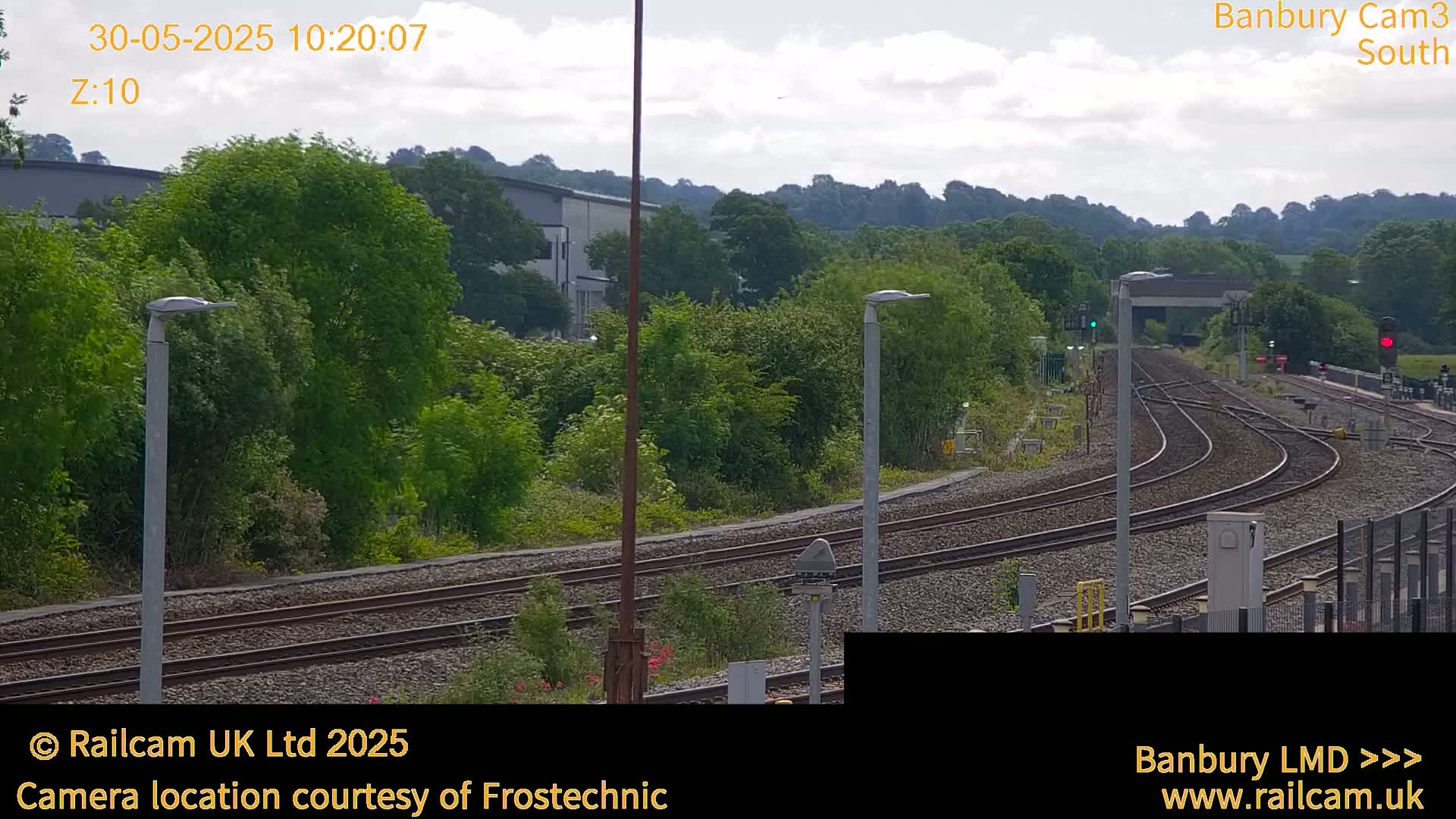 A view of a train track curving through a lush green landscape under a partly cloudy sky.