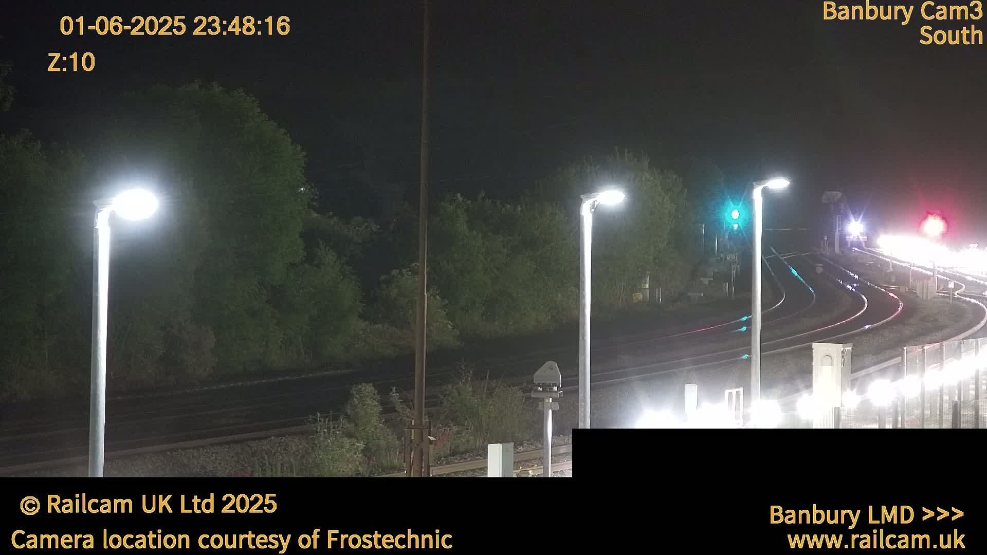A nighttime view of train tracks curving through a landscape of dark trees and lit by bright streetlights.