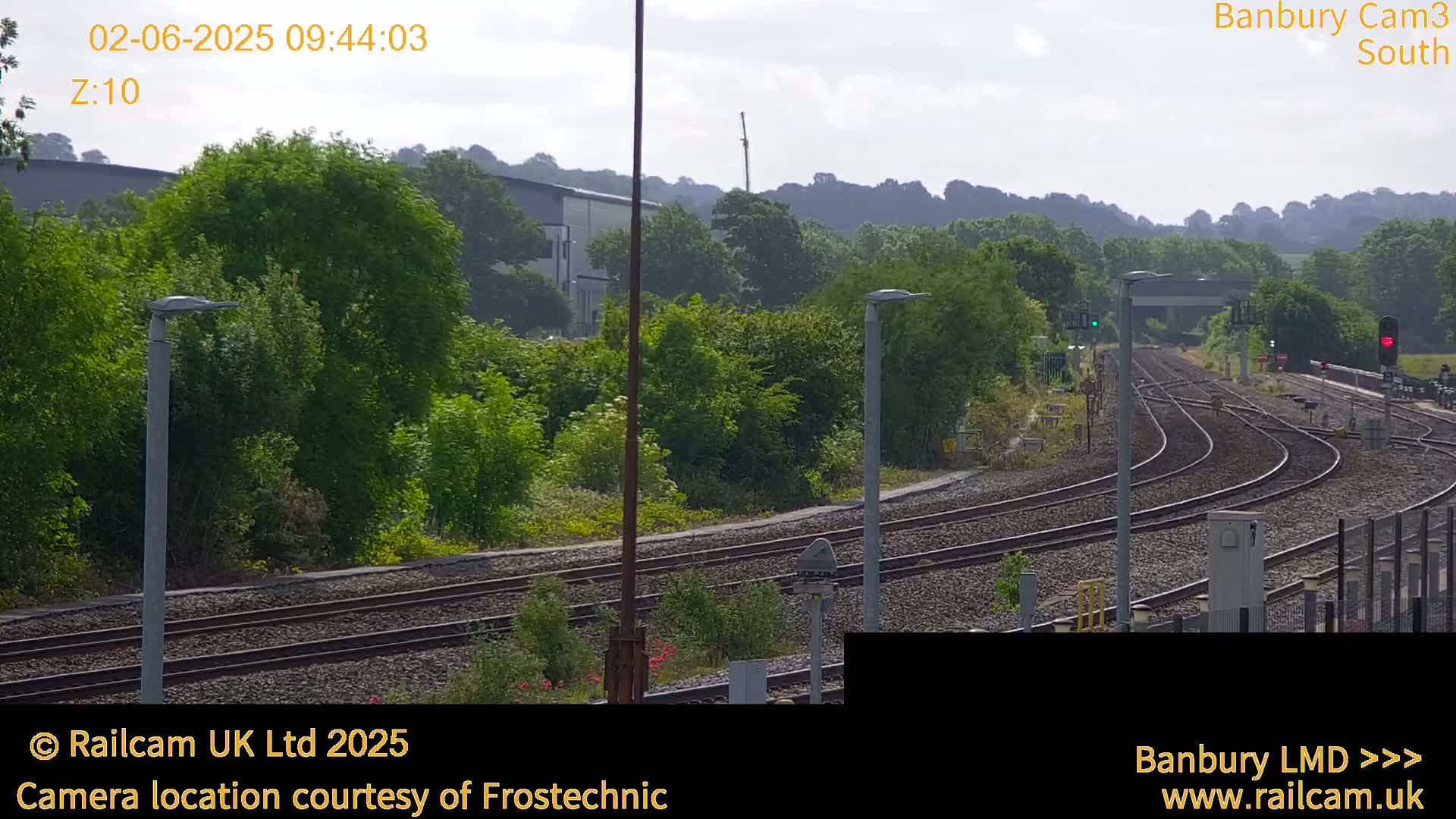 A view of a railway switching yard on a partly cloudy day, surrounded by lush green vegetation and hills in the distance.