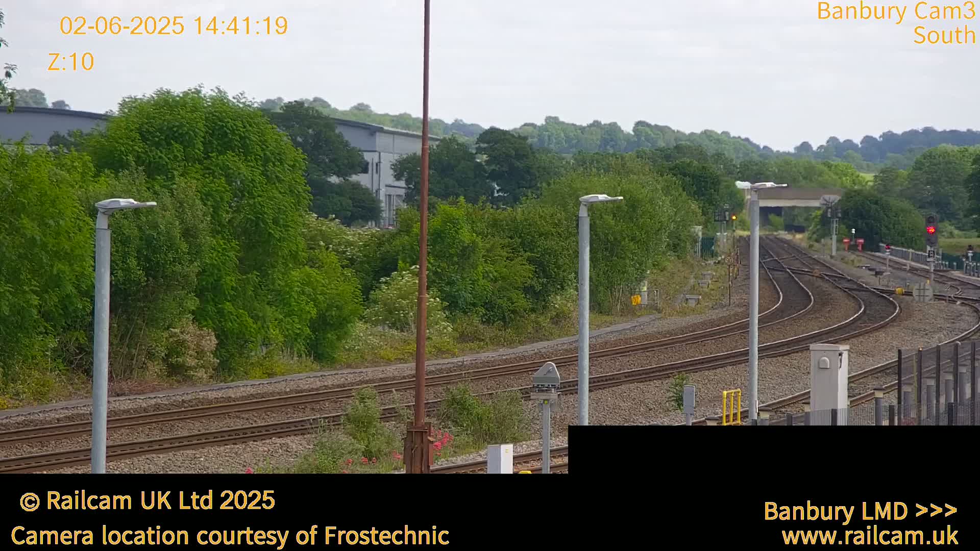 A view of train tracks curving through a lush green landscape under a partly cloudy sky.
