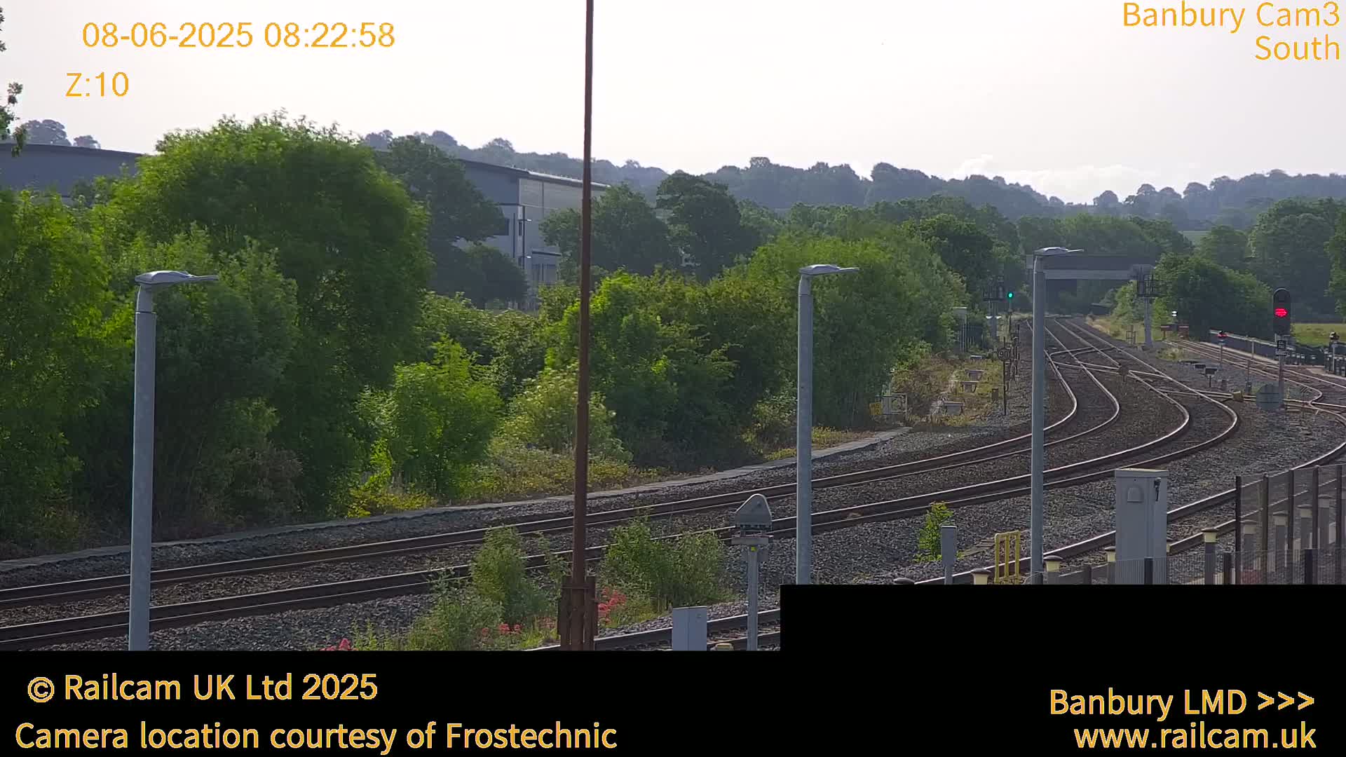 A view of a railway track system curving through a green landscape under a mostly clear sky.